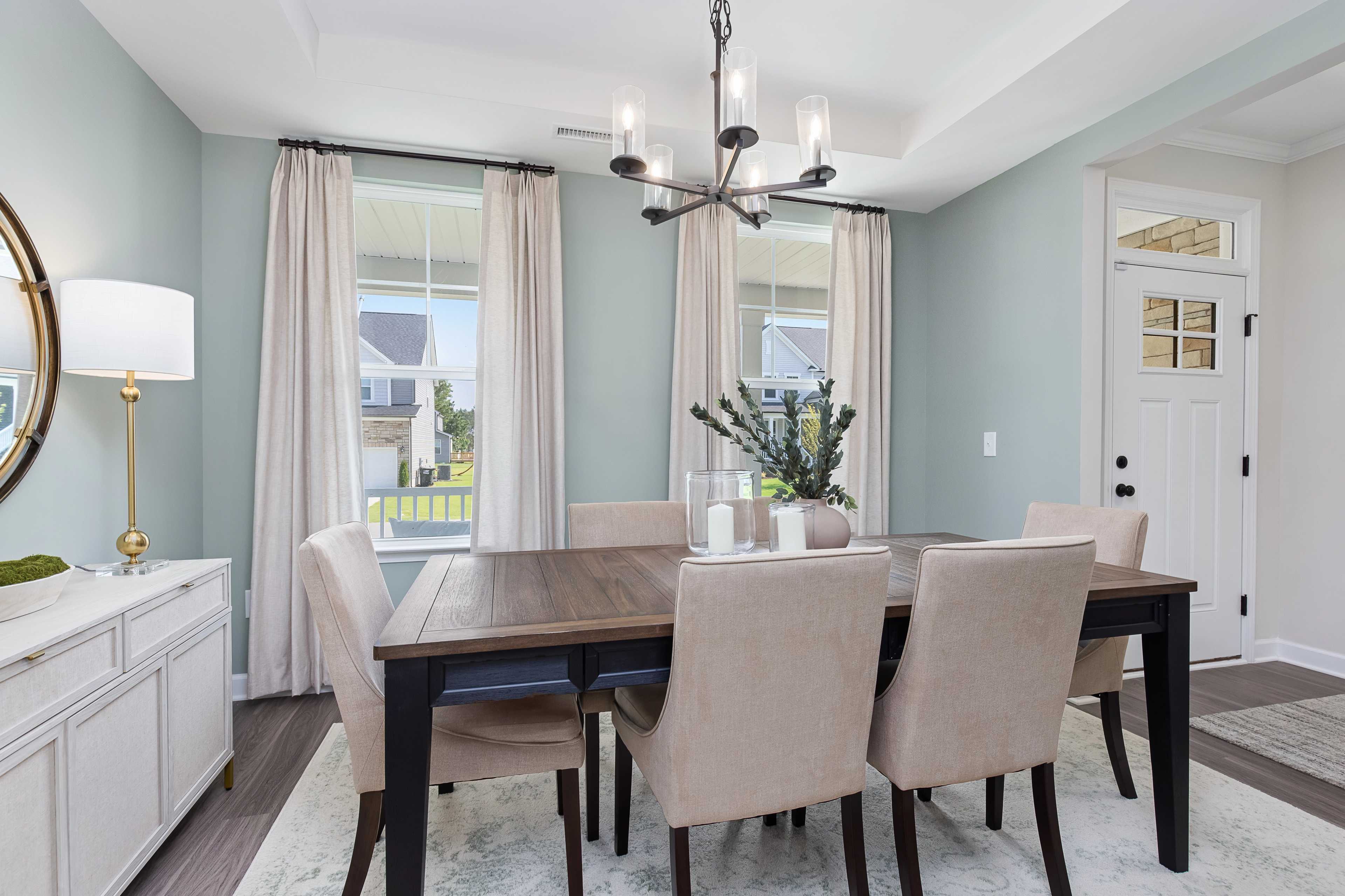 Dining room at Woodland Crossing in Zebulon NC by Davidson Homes with wooden table, beige chairs, chandelier, and large windows