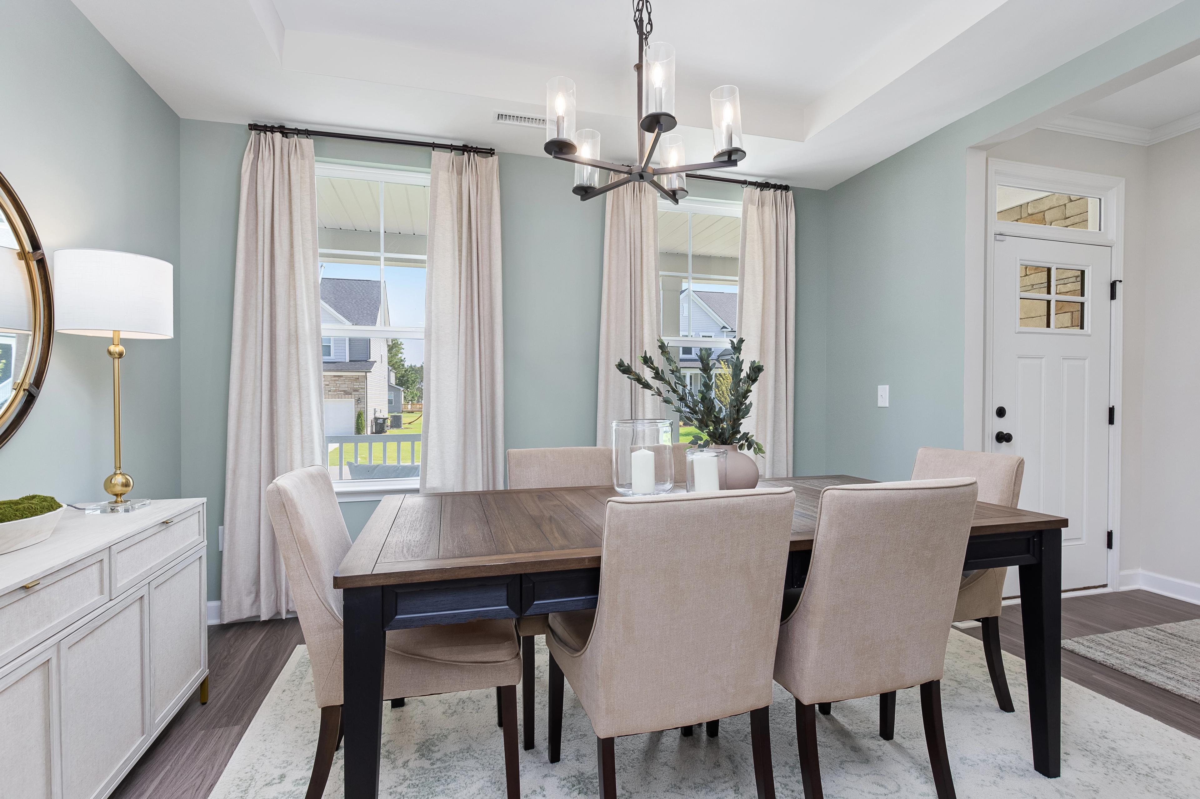 Dining room at Woodland Crossing in Zebulon NC by Davidson Homes with wooden table, beige chairs, chandelier, and large windows