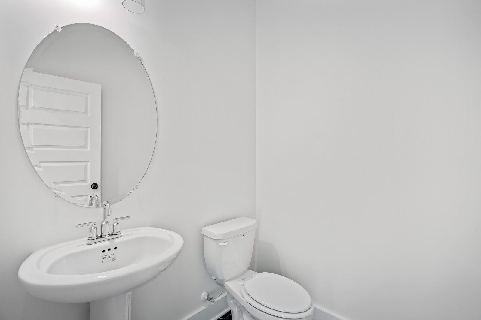 Bright white powder room with round mirror, pedestal sink, and toilet in Davidson Homes The Willow C, Gallatin, Tennessee