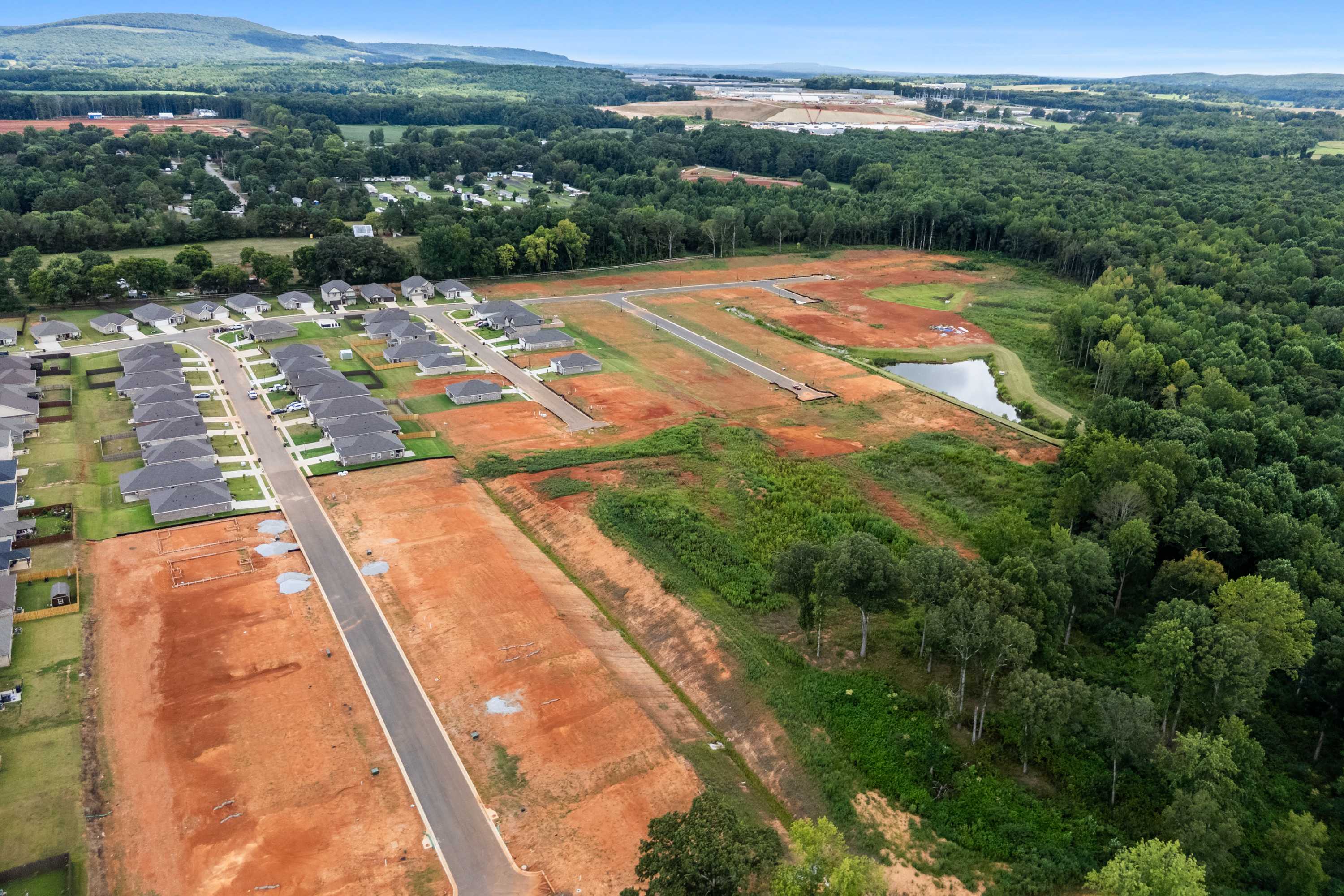 Aerial view of Wood Trail neighborhood in Toney Alabama with new homes, construction lots, pond, and wooded hills