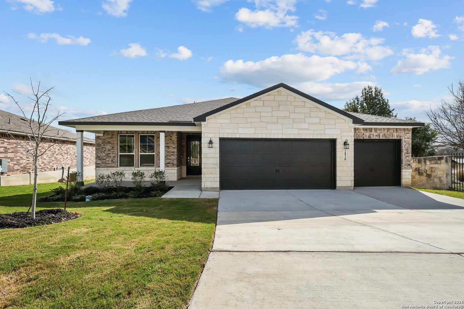 Modern single-story stone home with 3-car garage, covered porch, and lush front yard in Ladera, San Antonio, Texas - Davidson Homes The Lanier H