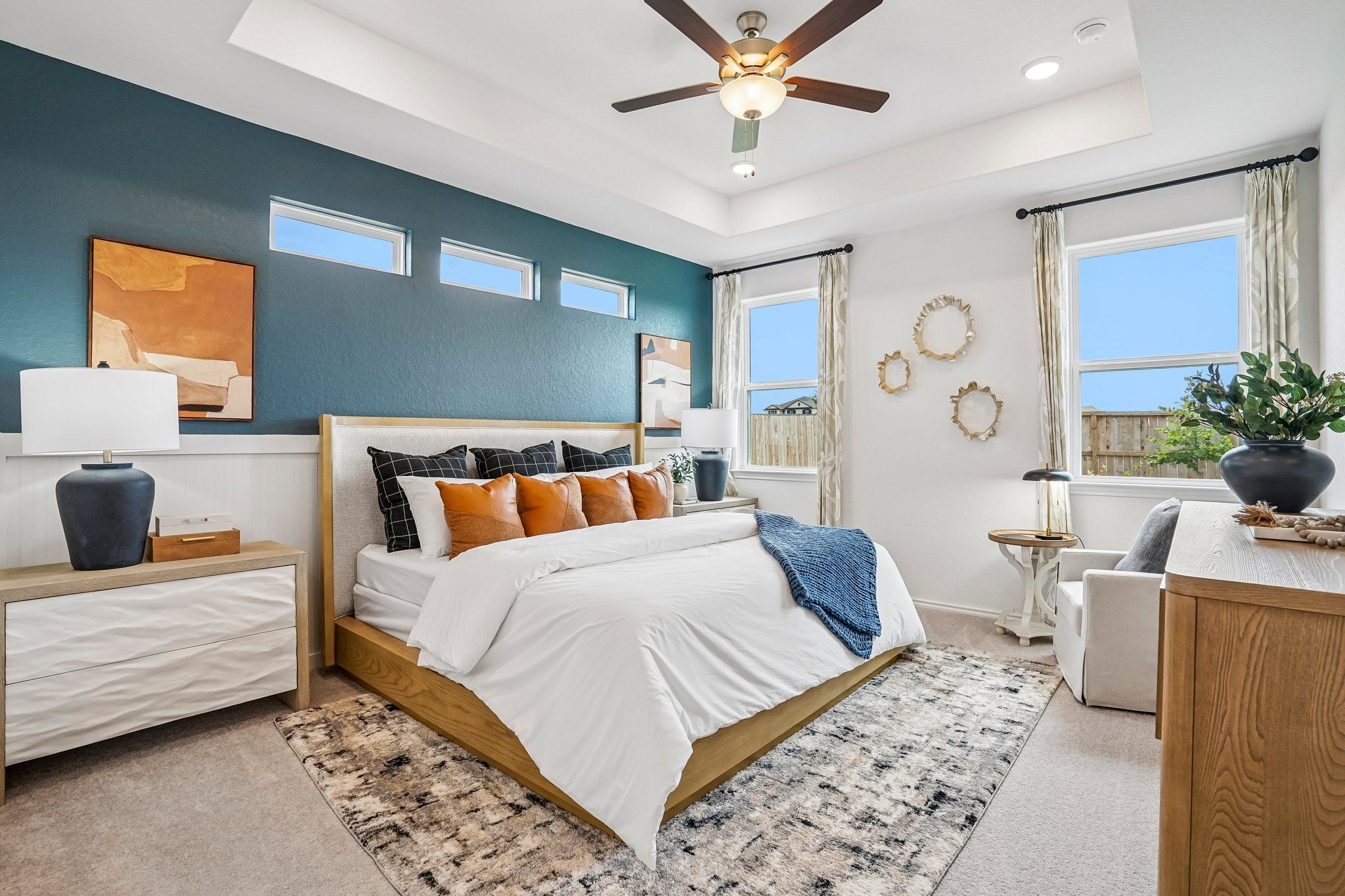 Spacious primary bedroom at Morgan Meadows in San Antonio with blue accent wall, tray ceiling, and modern wood furniture.