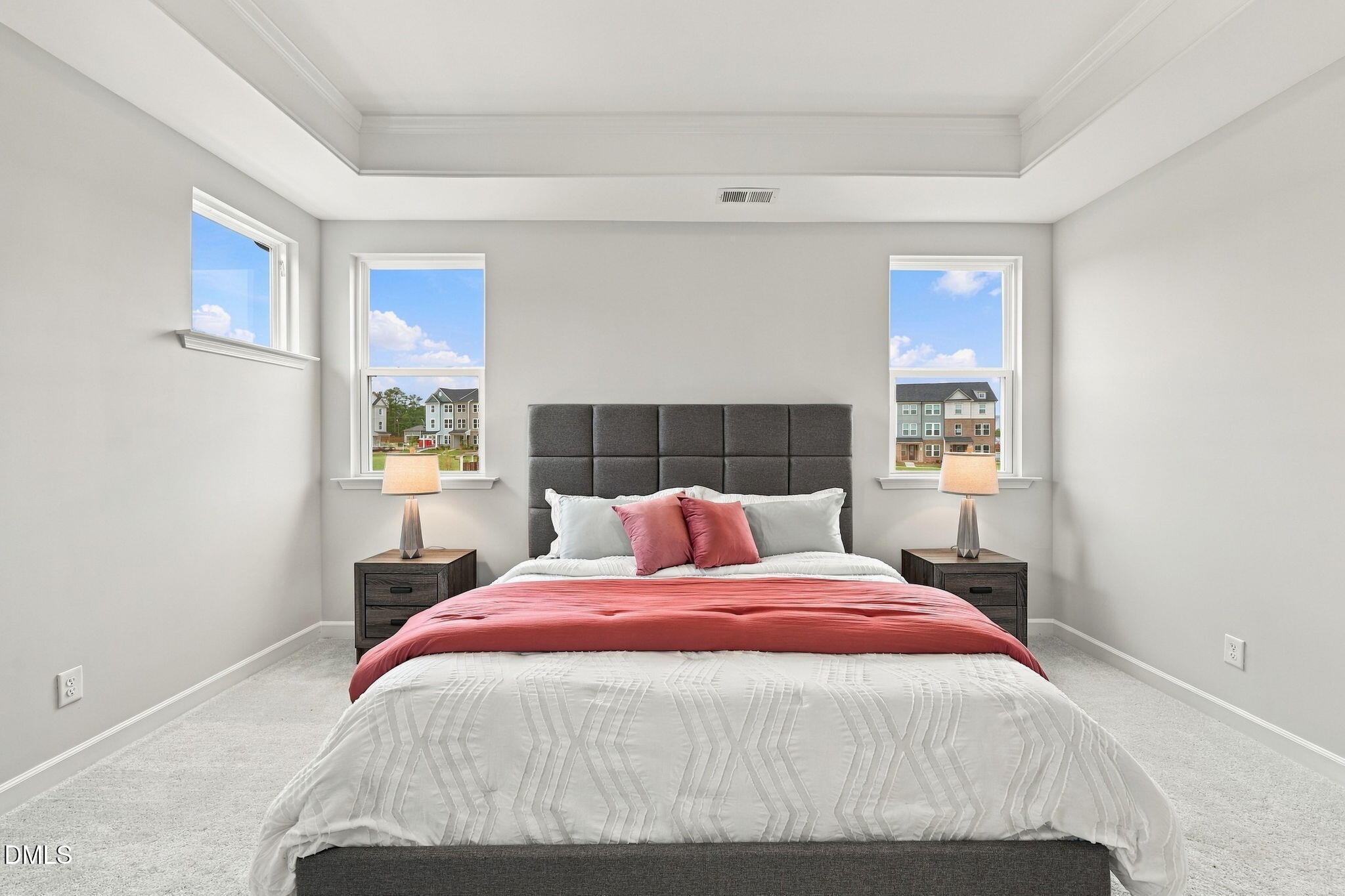 Bright primary bedroom with tray ceiling and gray upholstered headboard in Davidson Homes The Jordan C, Knightdale, NC
