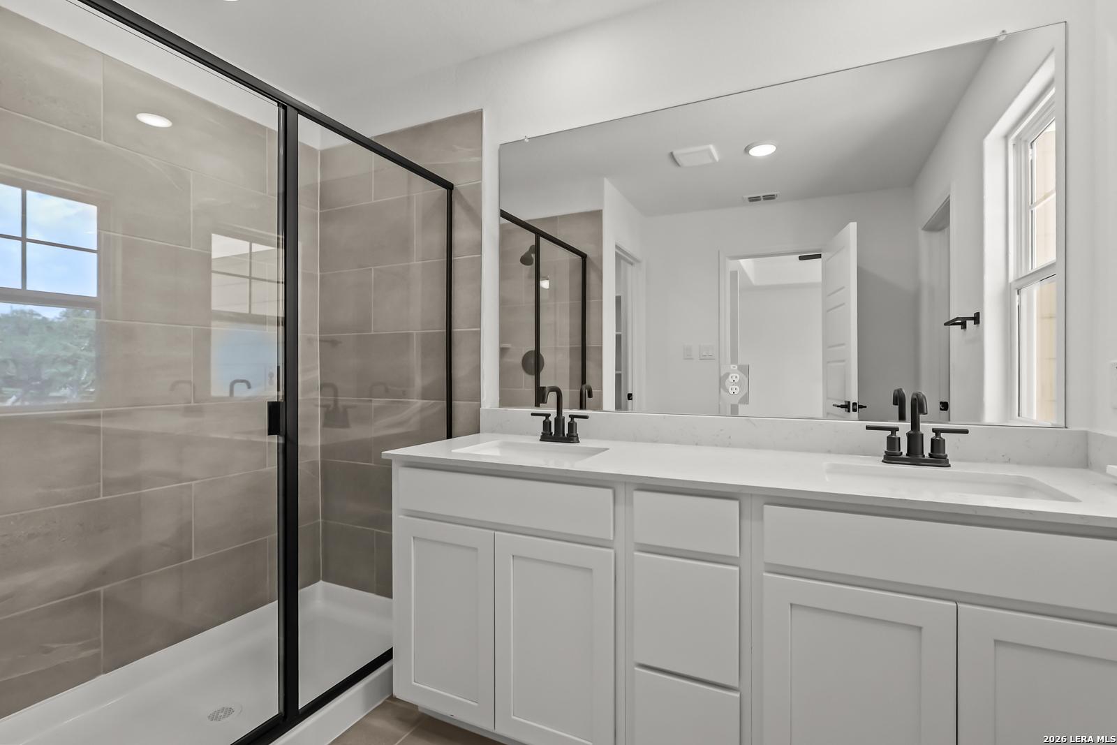 Modern bathroom with dual vanity and walk-in glass shower in The Florence B floor plan at Meadows at Oak Creek, San Antonio.