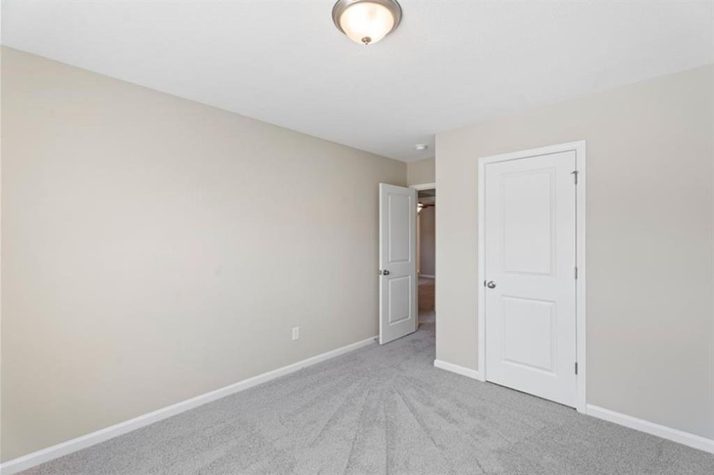 Secondary bedroom with beige walls, gray carpet, white doors, and ceiling light in Davidson Homes The Washington, Phenix City, Alabama
