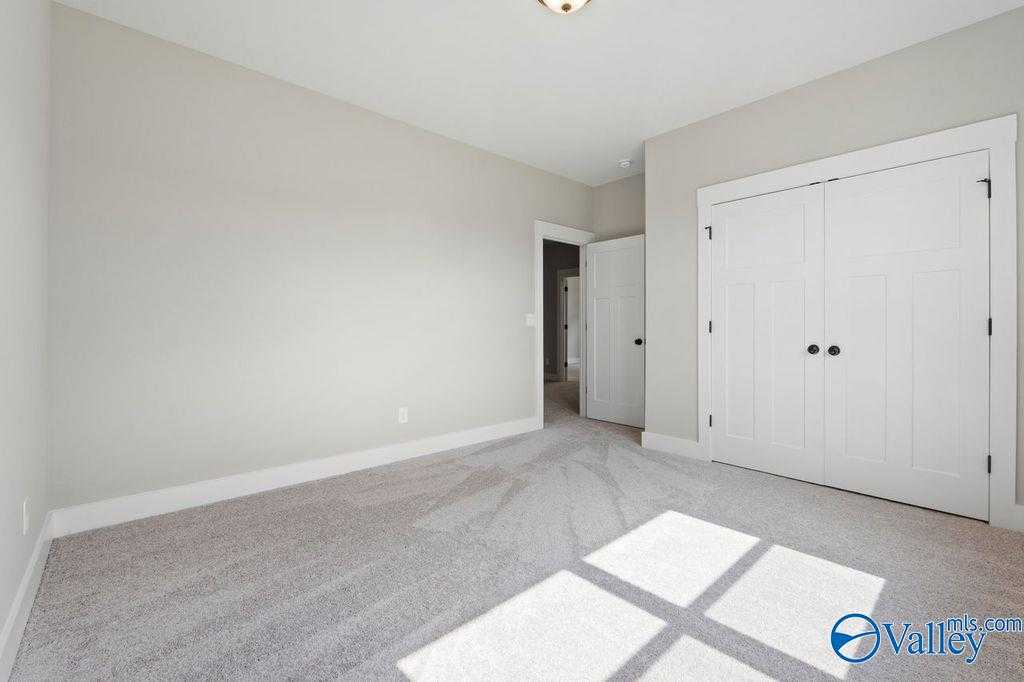 Spacious bedroom with light beige walls, double closet doors, and sunlit carpeted floor in Evermore Homes The Oxford, Owens Cross Roads, Alabama