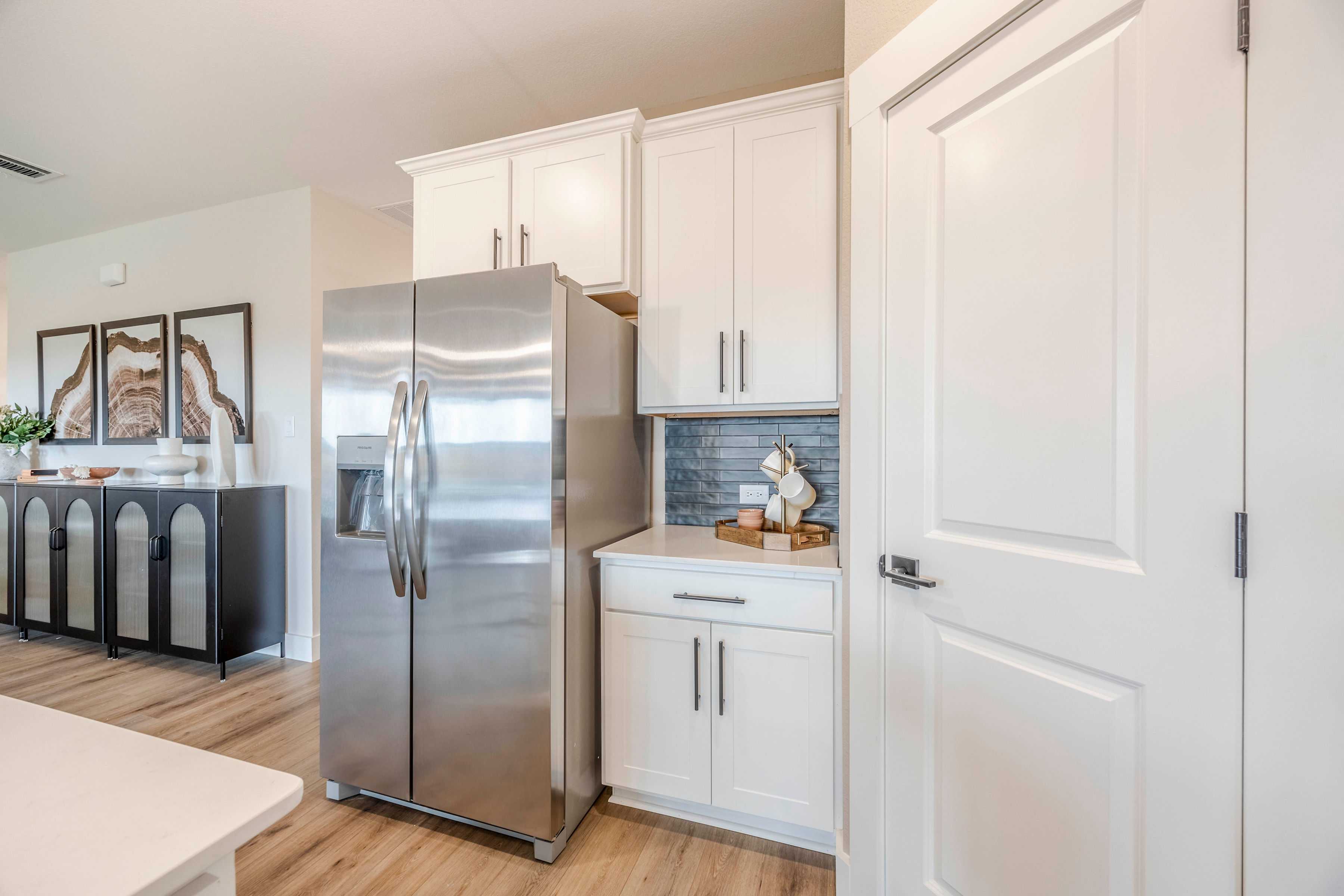 Modern kitchen in The Rockford by Davidson Homes with white shaker cabinets, stainless steel fridge, blue subway tile backsplash