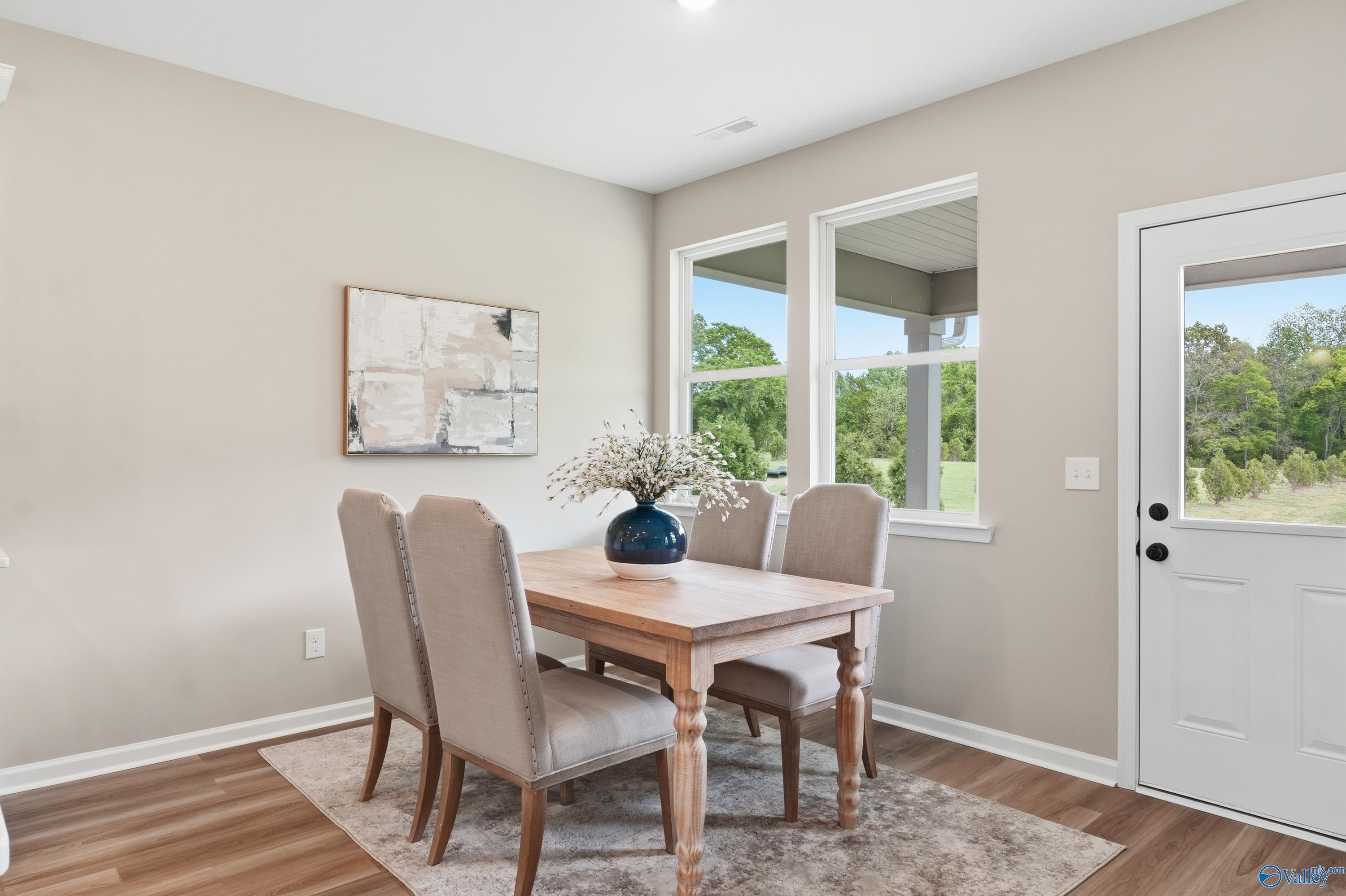 Elegant dining room with wooden table, tufted beige chairs, blue vase centerpiece, and backyard views in Davidson Homes The Dorado, Huntsville AL