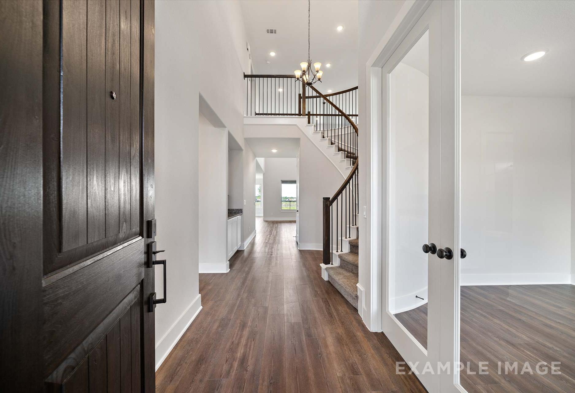 Spacious two-story foyer in The Victoria A showcasing open staircase, hardwood floors, chandelier, and glass doors