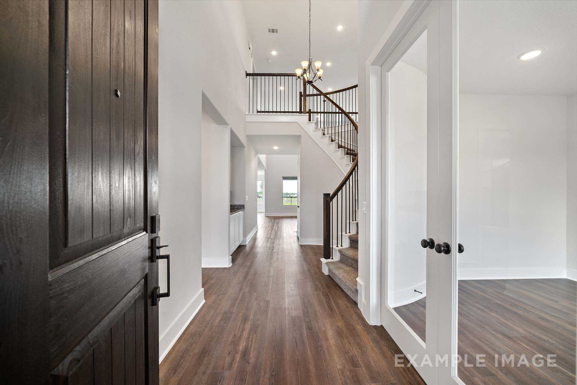 Spacious two-story foyer in The Victoria A showcasing open staircase, hardwood floors, chandelier, and glass doors