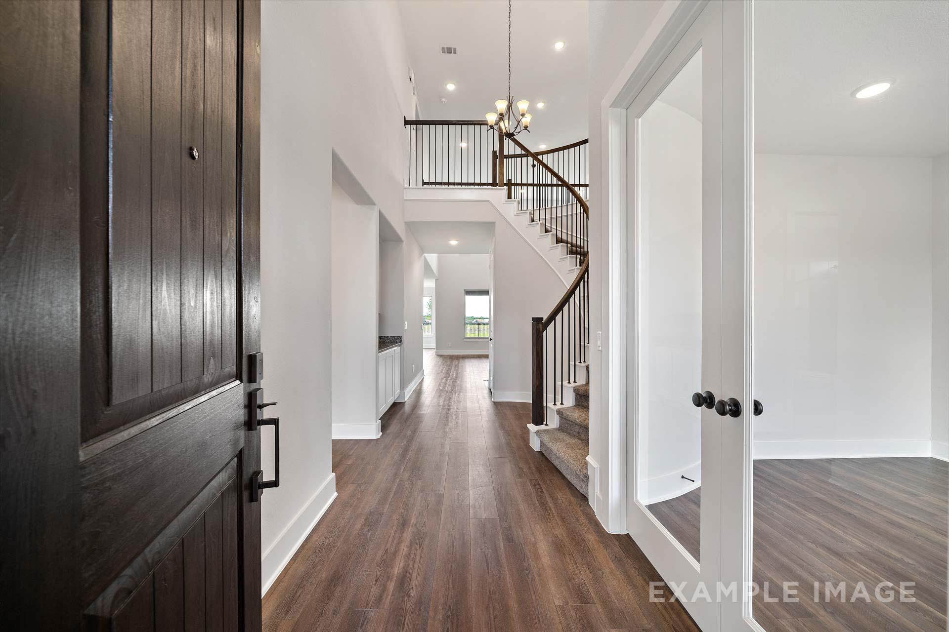 Spacious two-story foyer in The Victoria A showcasing open staircase, hardwood floors, chandelier, and glass doors