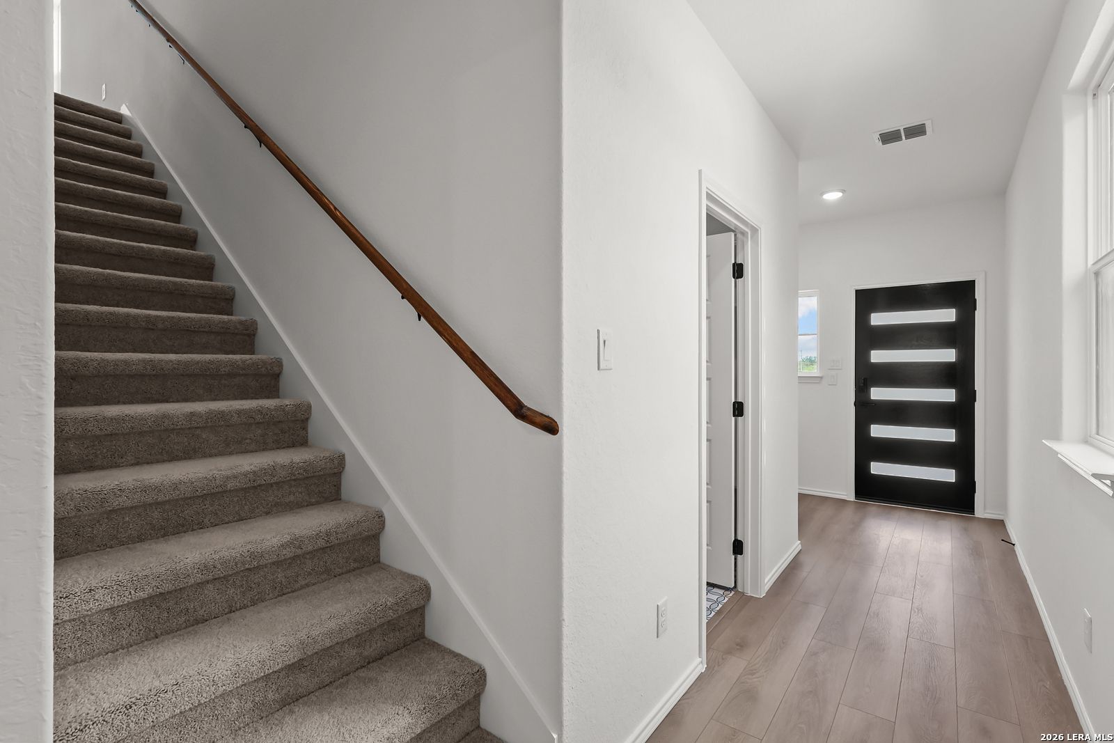 Carpeted staircase with wood handrail and wood-look flooring in 2-story Davidson Homes foyer at Morgan Meadows, San Antonio, Texas