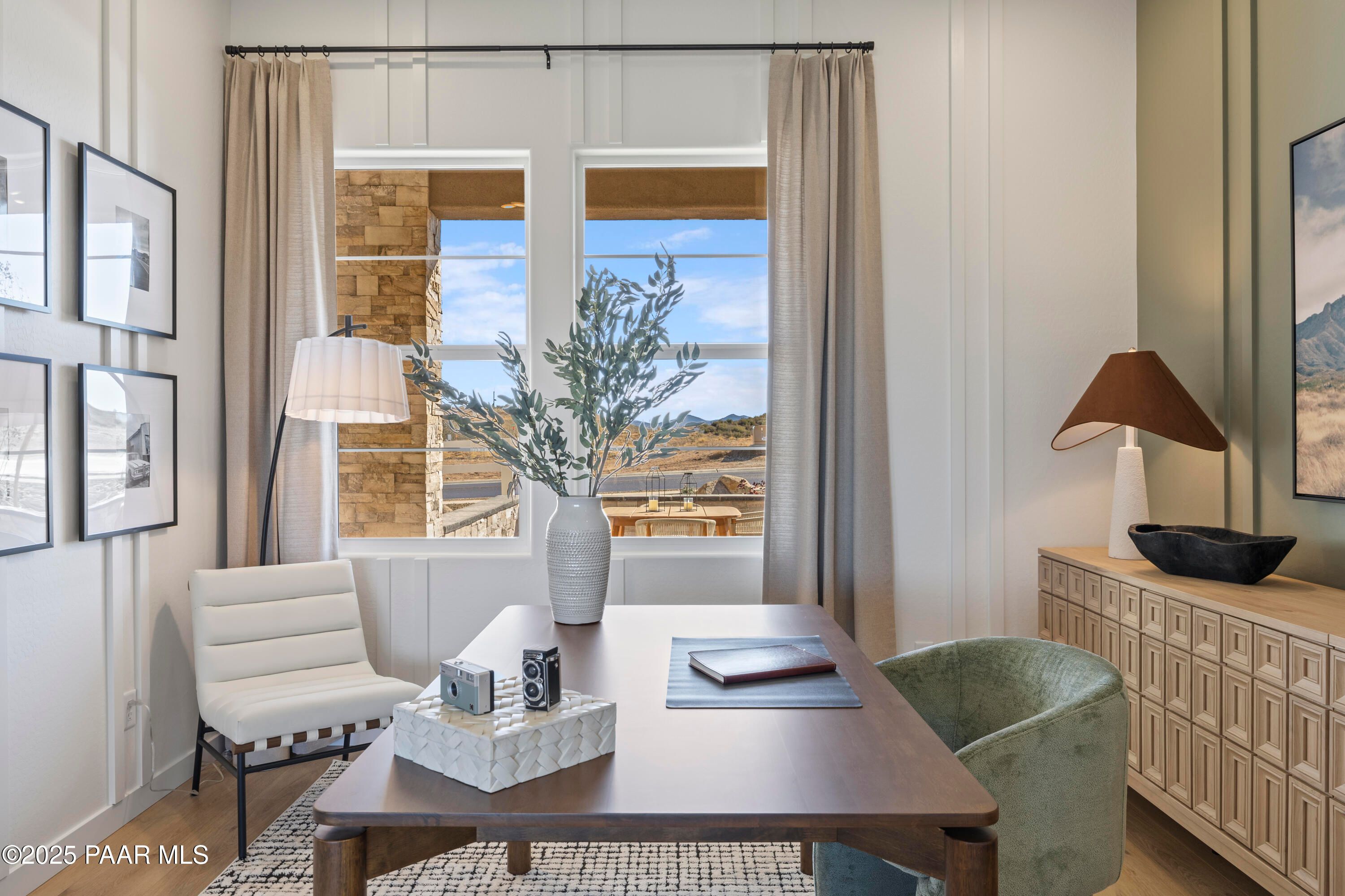 Modern home office with wooden desk, green armchair, mountain view windows, and potted olive branch in Davidson Homes The Blaze D, Prescott, Arizona