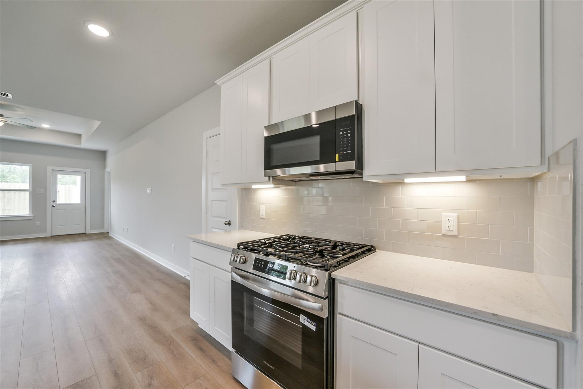 Modern white kitchen with stainless steel gas range, oven, and microwave in The Frio F floor plan, Conroe, Texas