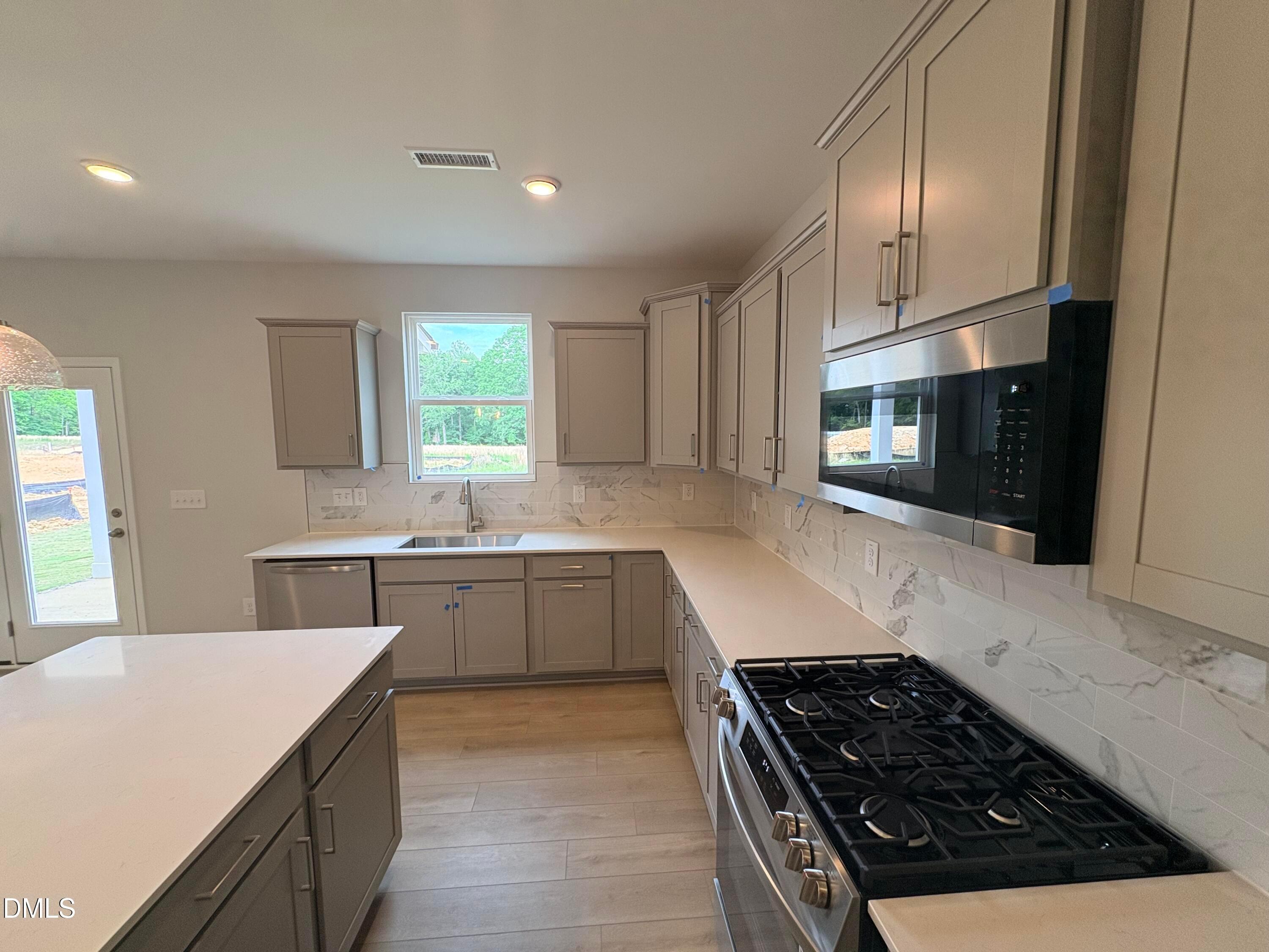 Modern kitchen with gray cabinets, quartz countertops, and stainless steel appliances in The Hickory II C, Zebulon, NC.