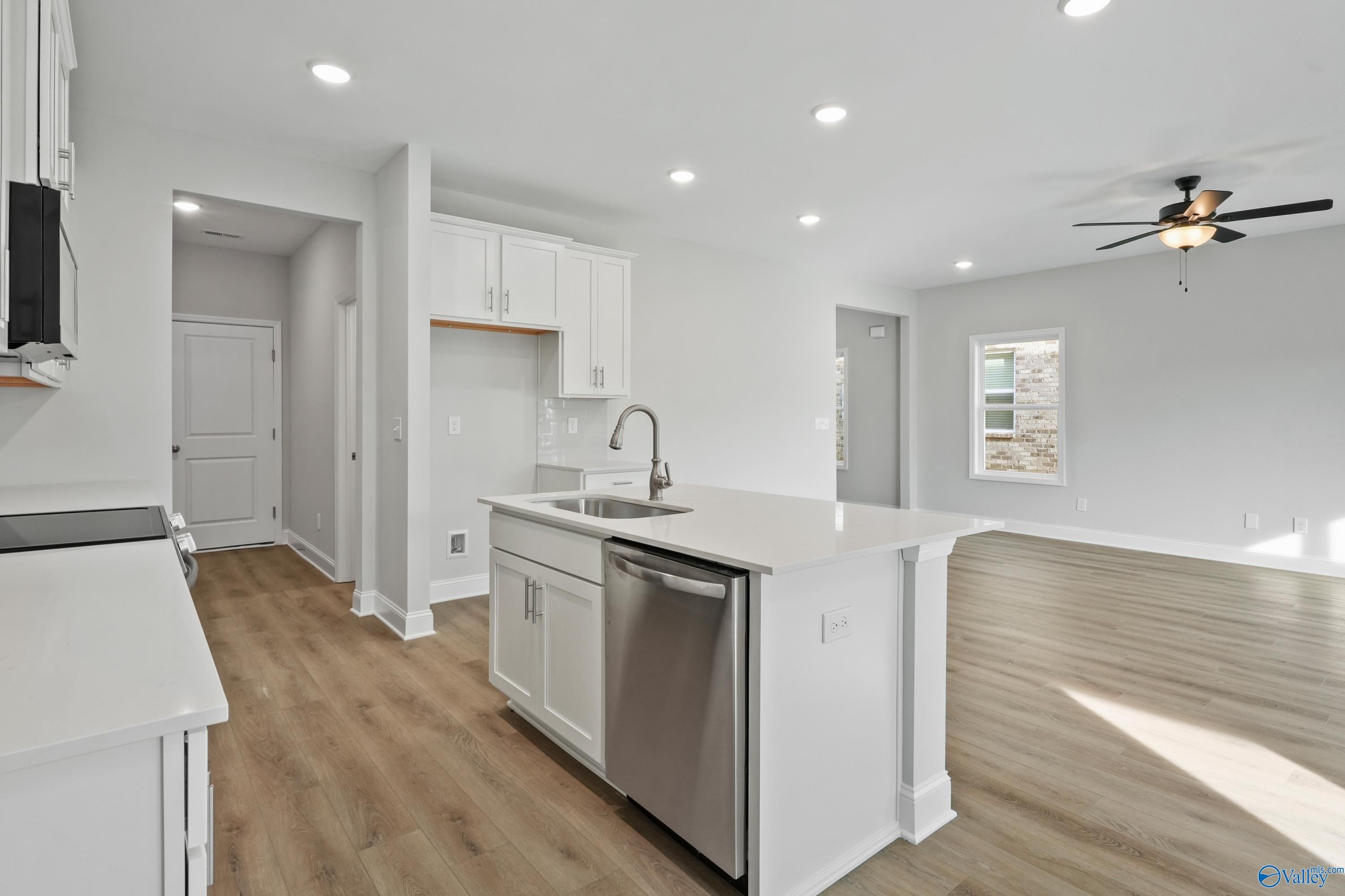 Modern white kitchen island with sink, stainless dishwasher, and open layout in Davidson Homes The Camden, Huntsville AL