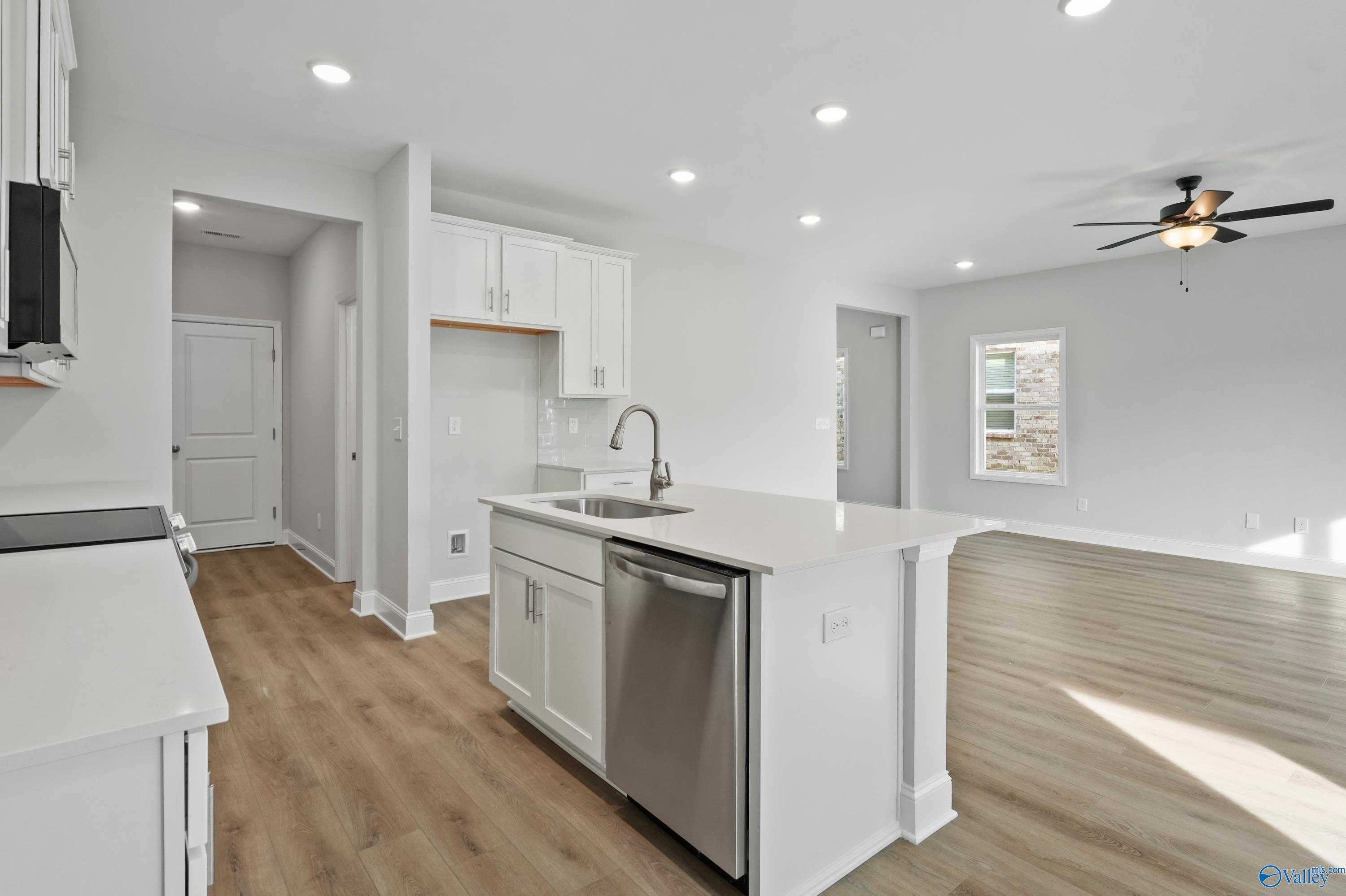 Modern white kitchen island with sink, stainless dishwasher, and open layout in Davidson Homes The Camden, Huntsville AL