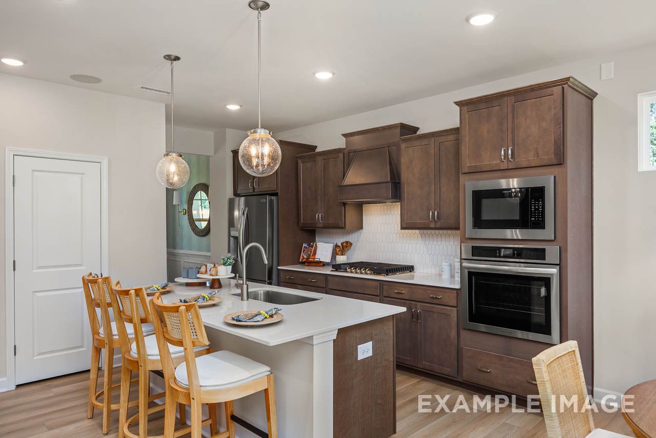 Gourmet kitchen in The Willow C-BF by Davidson Homes featuring dark wood cabinetry, white island with seating, and stainless appliances.