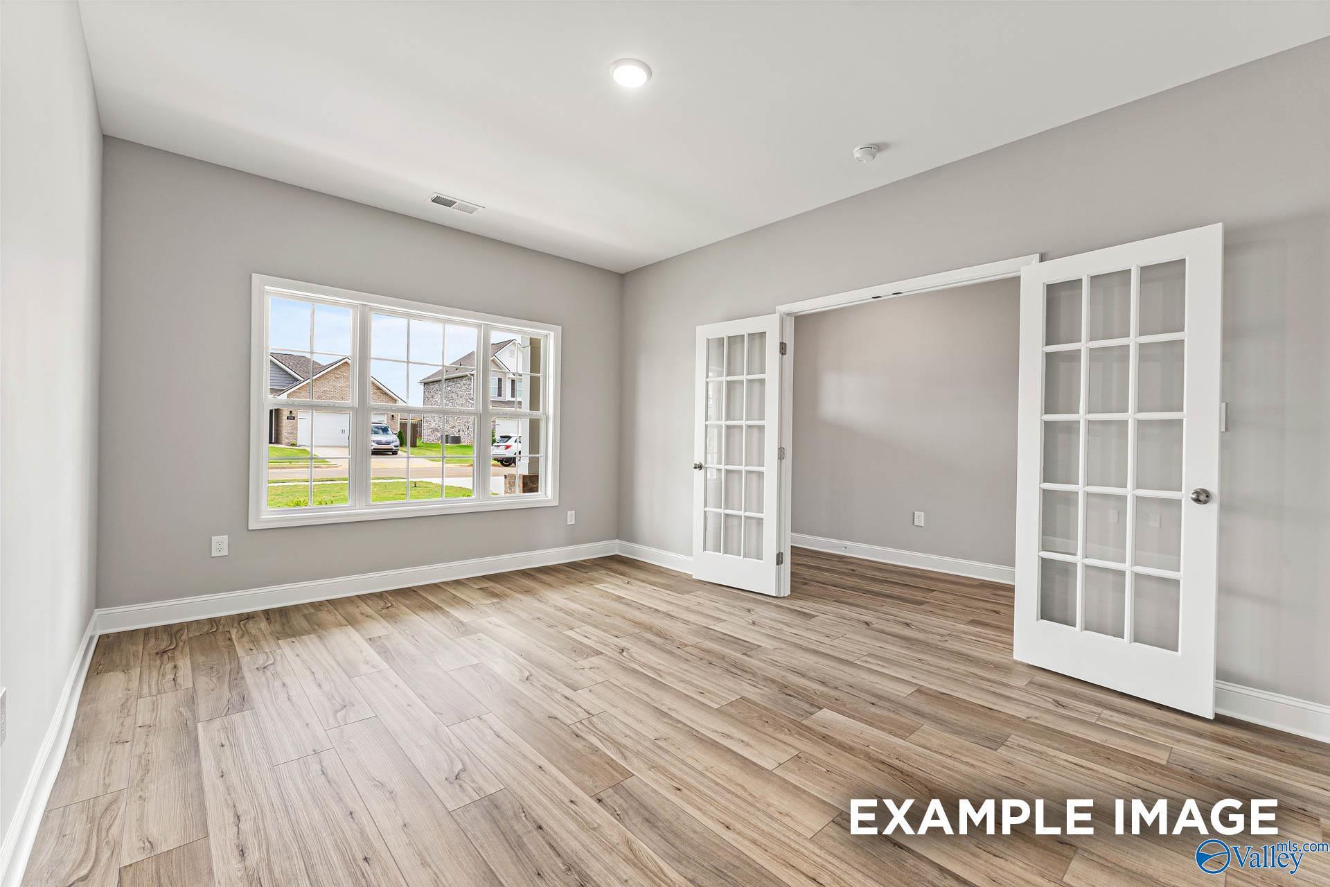Bright empty room with light gray walls, large window to neighborhood view, open French doors, hardwood floors in Davidson Homes Chelsea B, Toney AL