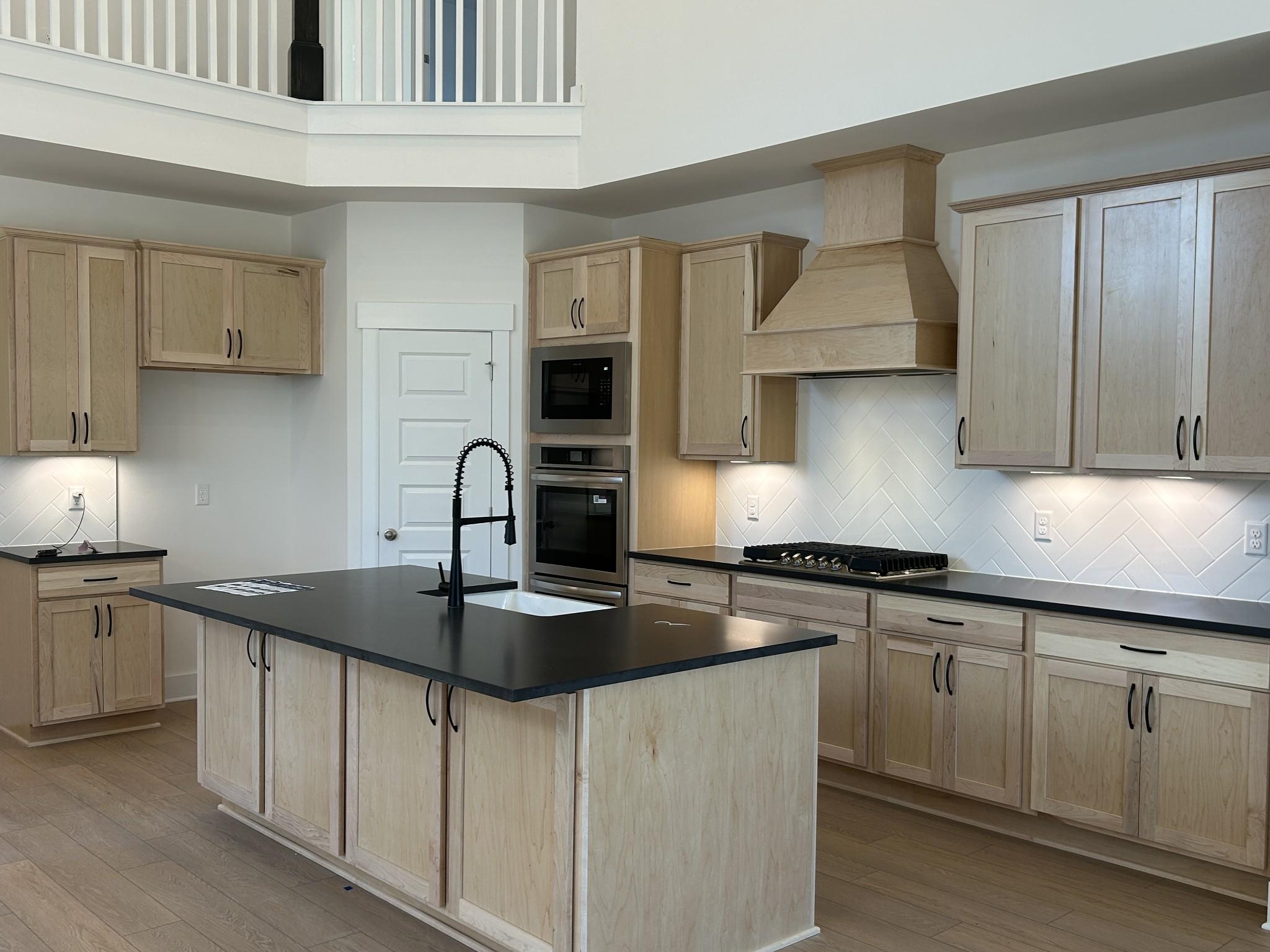 Modern kitchen featuring light oak cabinets, black granite island, double oven, and gas cooktop in Davidson Homes The Ridgeport E, Mt. Juliet, TN