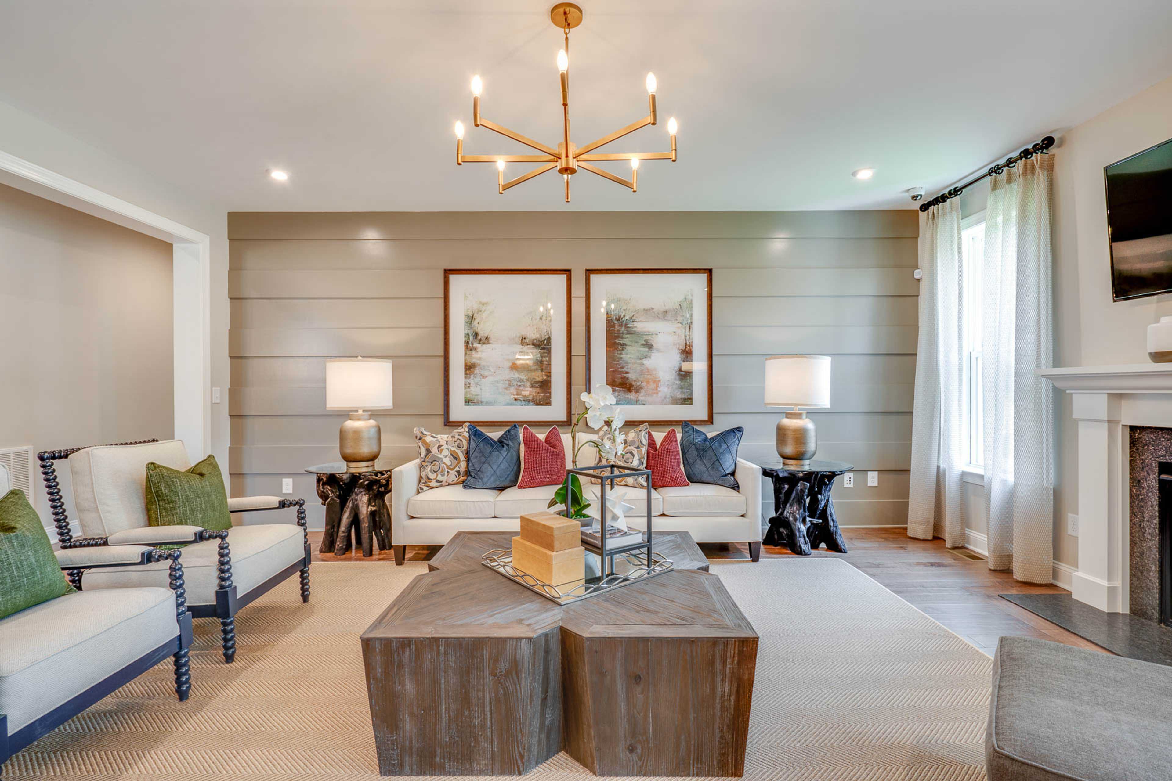 Cozy living room in Hasentree featuring shiplap accent wall, modern chandelier, plush sofa, coffee table, and fireplace in Wake Forest NC