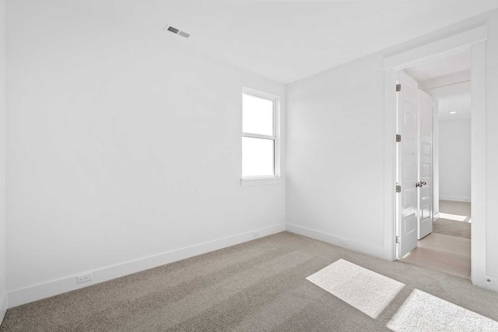 Bright empty bedroom with white walls, carpeted floor, window, and open door in Davidson Homes The Alston A, Murfreesboro, TN
