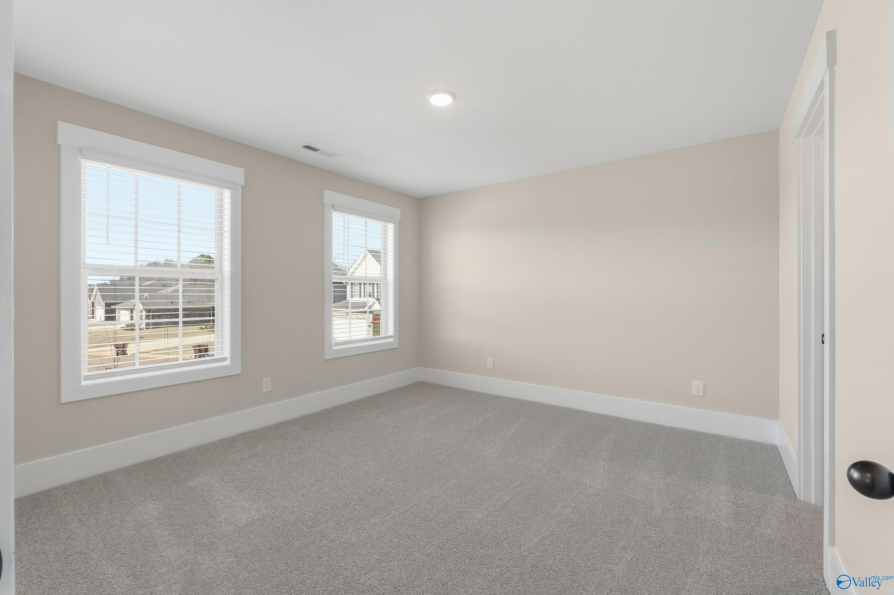 Bright empty bedroom with large windows, beige walls, and plush carpet in The Shelby A, Davidson Homes, Athens, Alabama