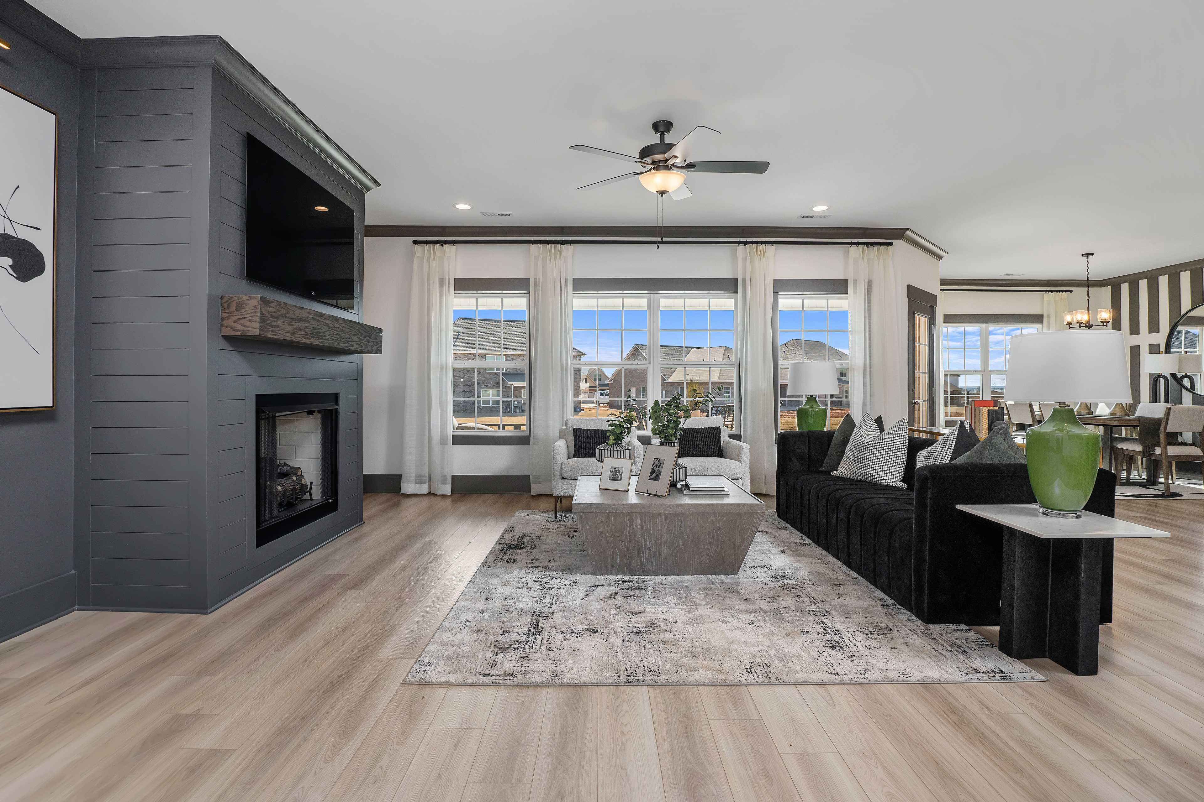 Open-concept living room at Barnett's Crossing in Madison Alabama with stone fireplace, black velvet sofa, hardwood floors, and large windows