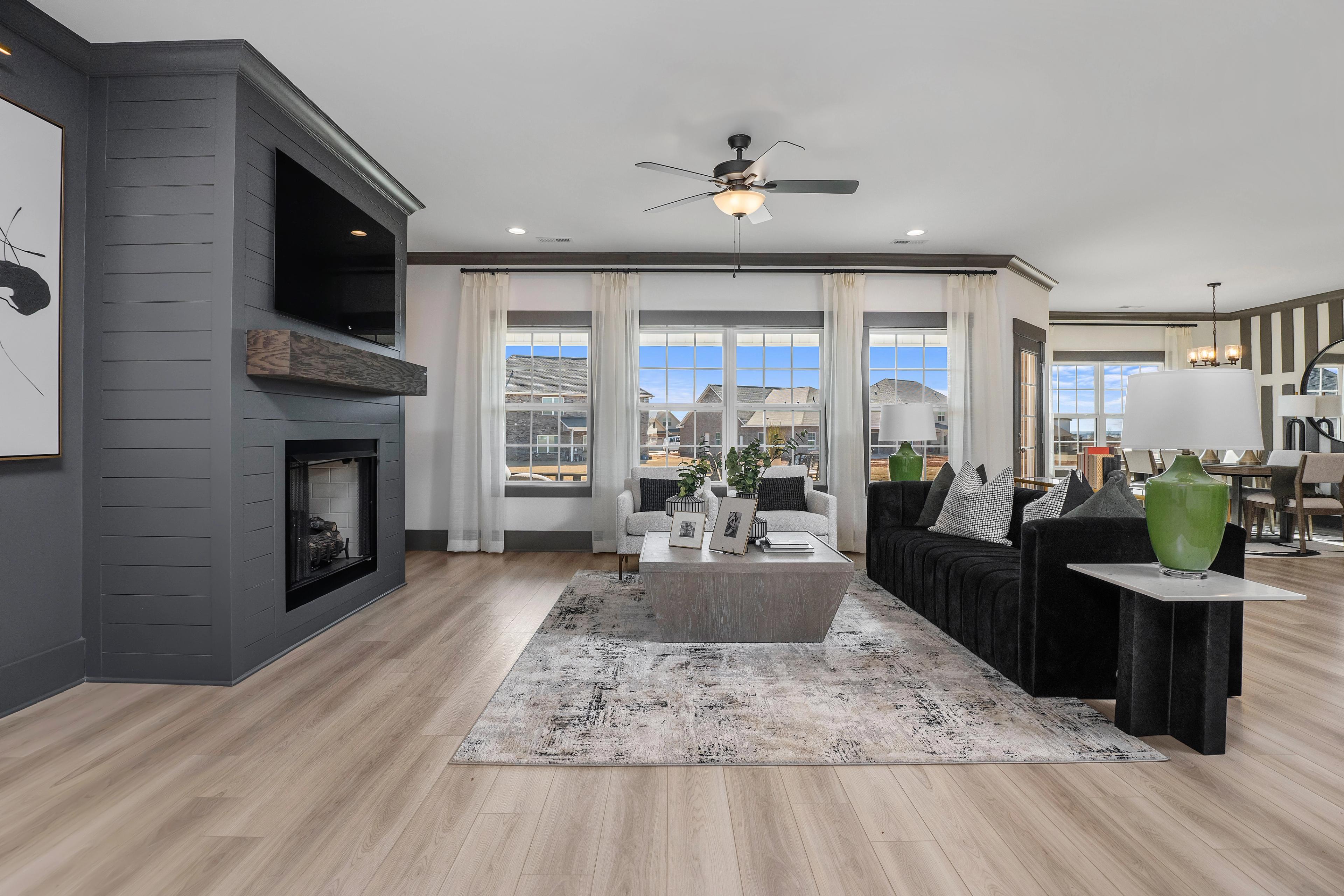 Open-concept living room at Barnett's Crossing in Madison Alabama with stone fireplace, black velvet sofa, hardwood floors, and large windows