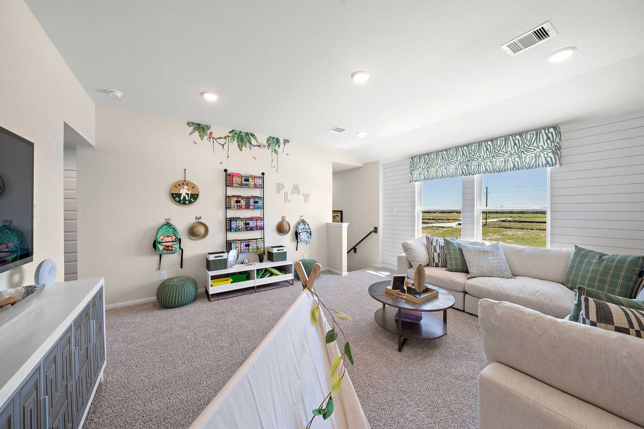 Spacious loft playroom at River Ranch Meadows in Dayton TX by Davidson Homes with sectional sofa, built-in shelves, and scenic field views