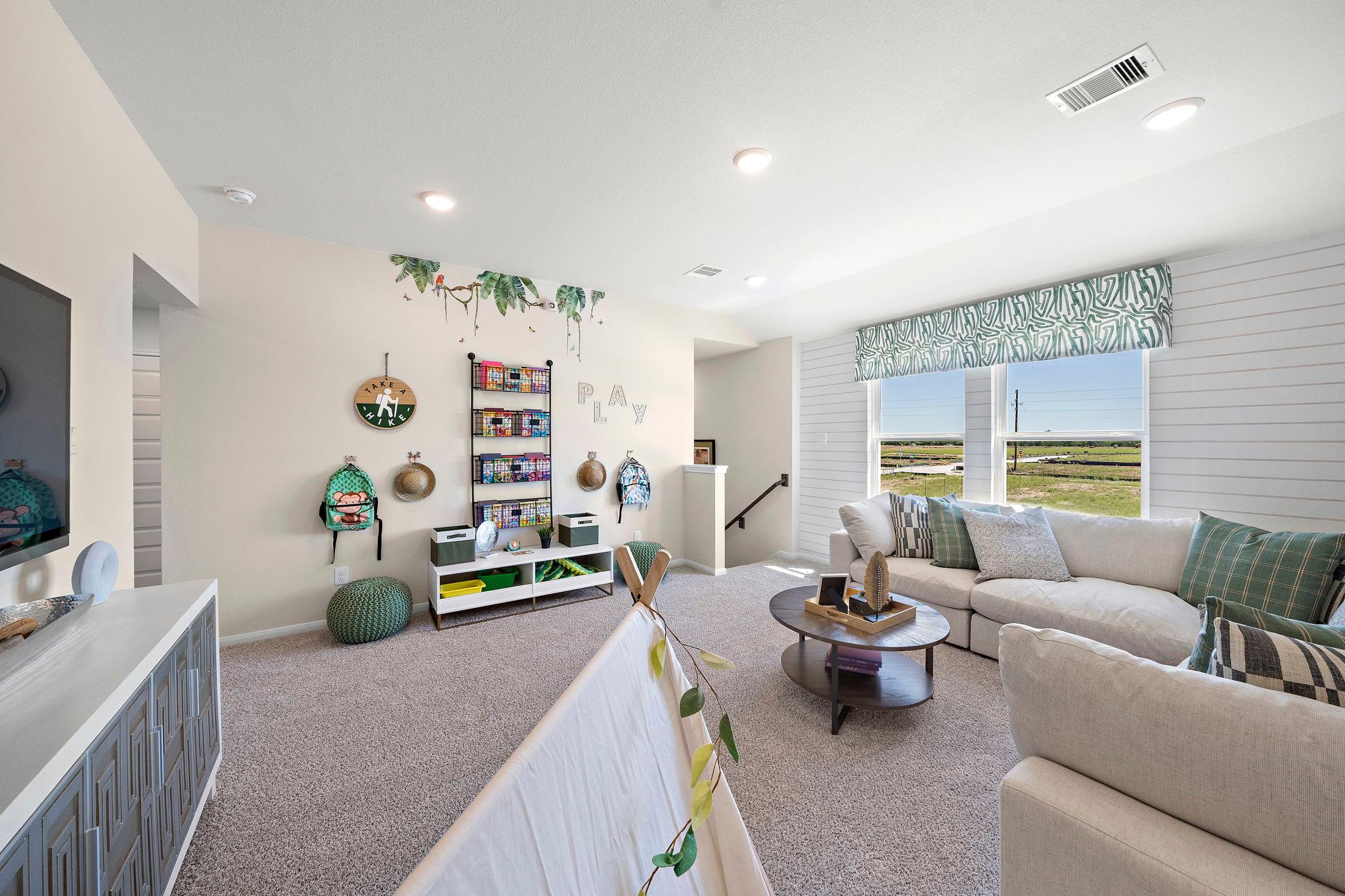 Spacious loft playroom at River Ranch Meadows in Dayton TX by Davidson Homes with sectional sofa, built-in shelves, and scenic field views