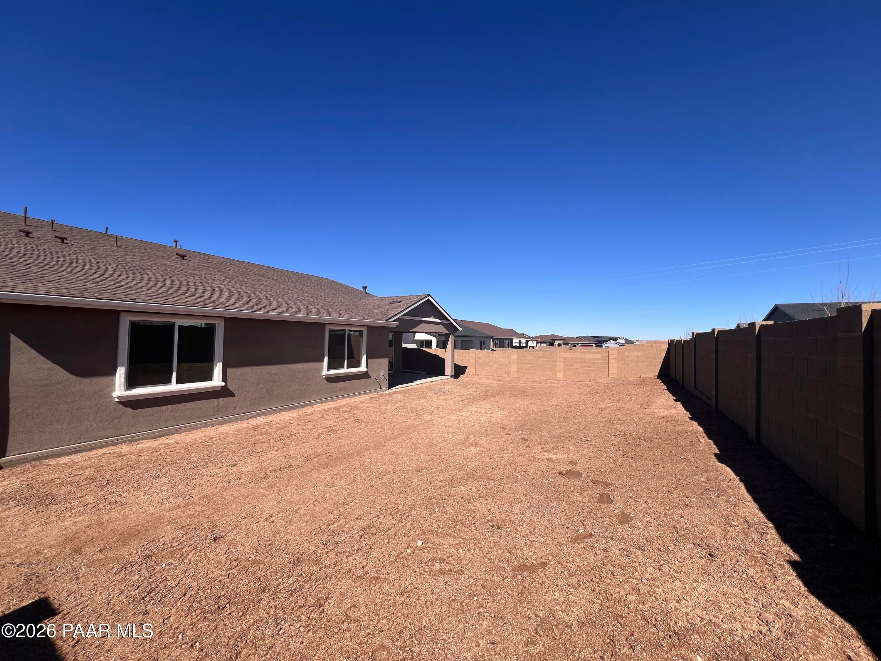 Tan stucco 1-story home with 3-car garage, spacious gravel side yard, and block fence in Westwood, Prescott, Arizona