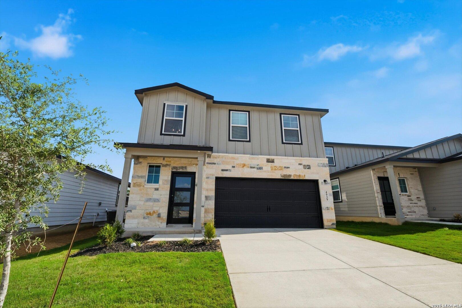 Modern 4-bedroom single-story home with gray siding, stone facade, black 2-car garage, driveway, and lush lawn in Agave, San Antonio, Texas