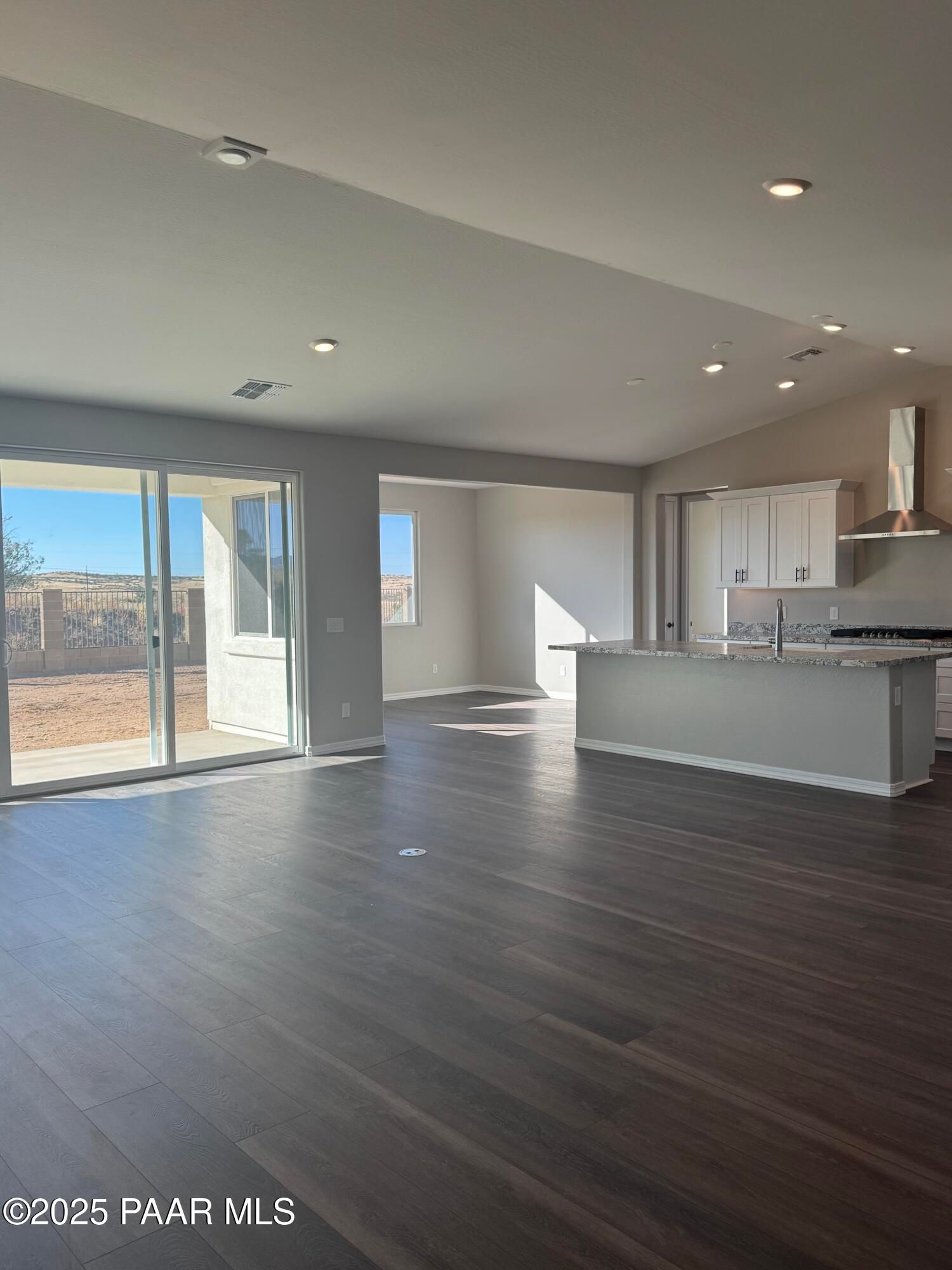 Open-concept kitchen and living space with white cabinets, island, and sliding doors to desert view in The Monarch E, Prescott, Arizona