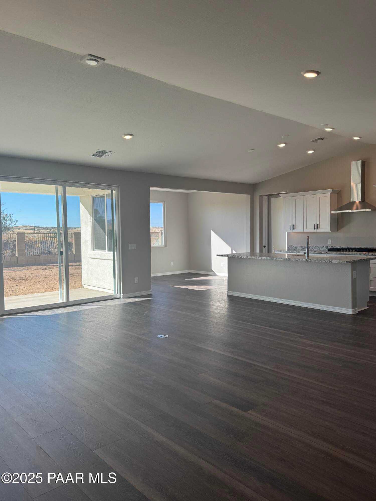 Open-concept kitchen and living space with white cabinets, island, and sliding doors to desert view in The Monarch E, Prescott, Arizona