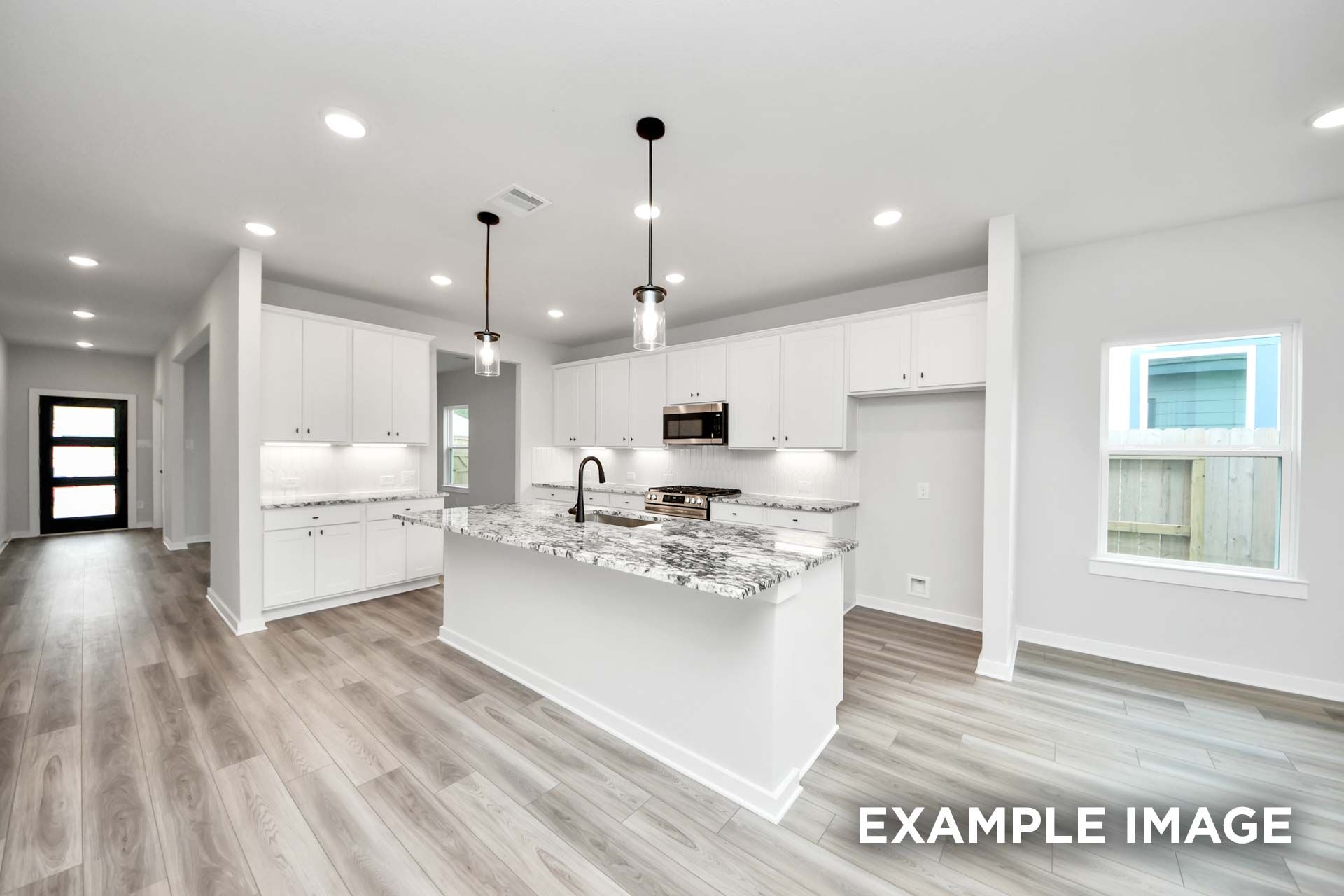 Modern white kitchen in The Sorrento F featuring a granite island, pendant lighting, and sleek wood-look flooring.