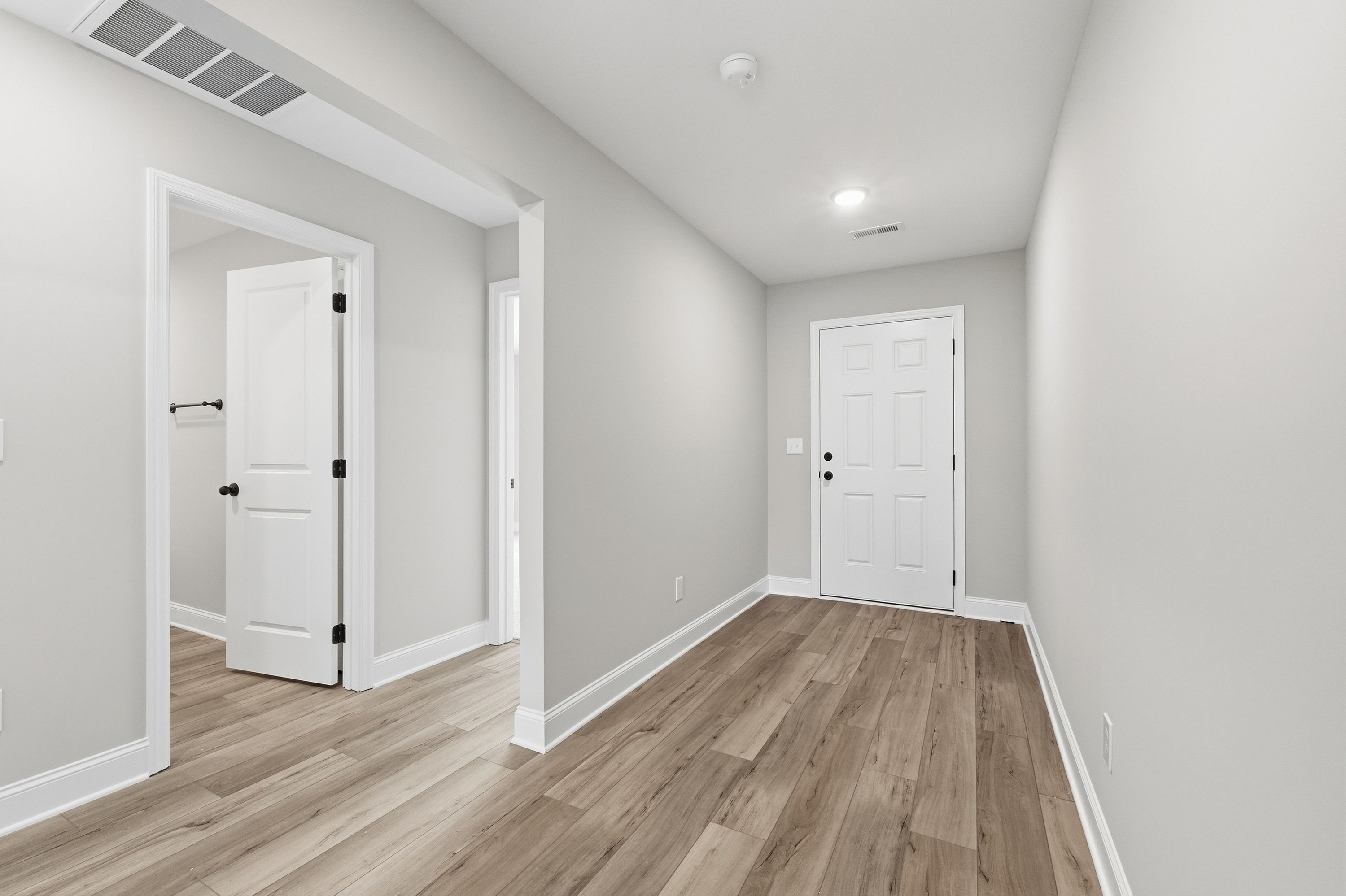 Spacious hallway in The Daphne V home featuring light gray walls, white paneled doors, open archway, and warm hardwood floors