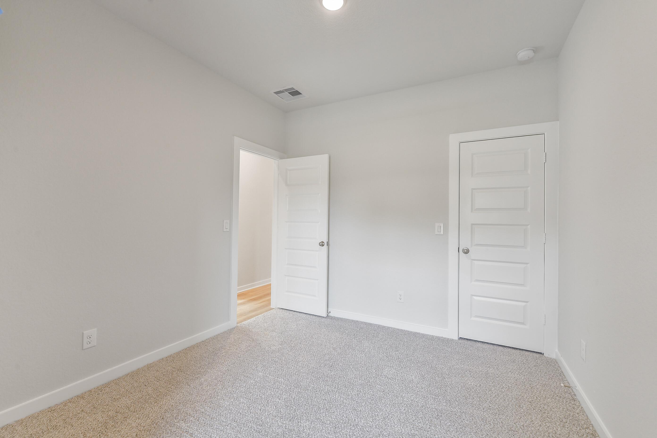 Spacious secondary bedroom with gray carpet, neutral walls, white paneled doors, and hallway access in Davidson Homes Colorado G, Magnolia TX