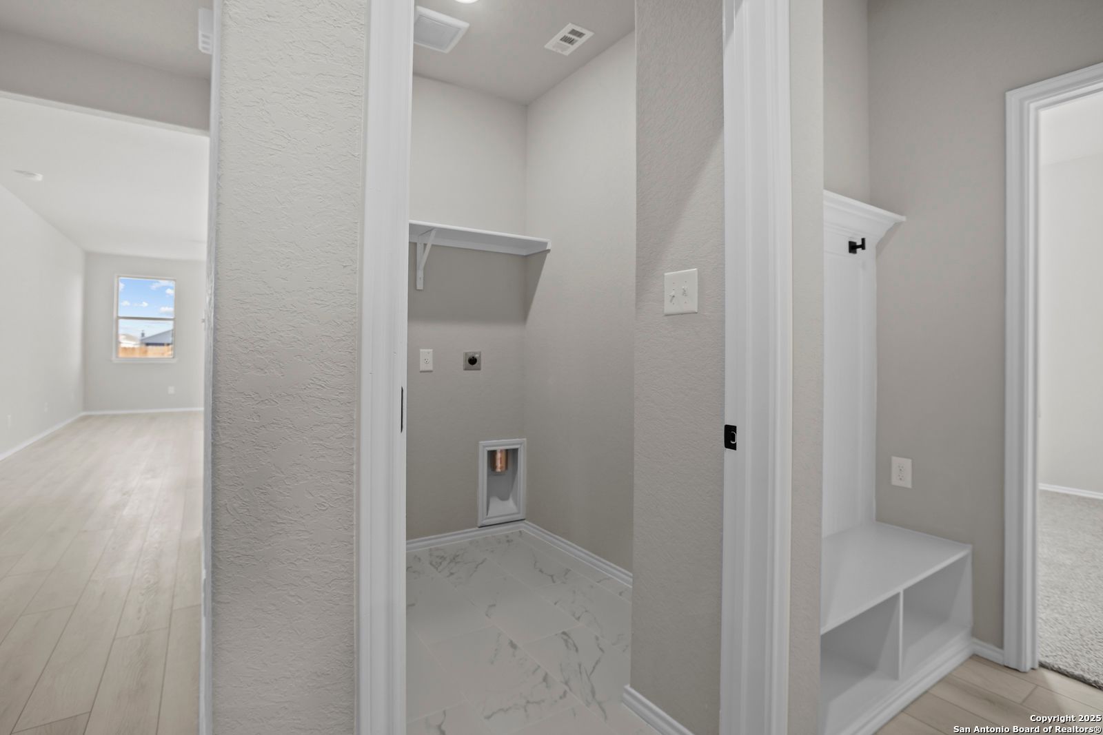 Functional laundry room with washer-dryer hookups, utility sink, built-in storage, bench, and hooks in Davidson Homes The Daphne H, Seguin, Texas