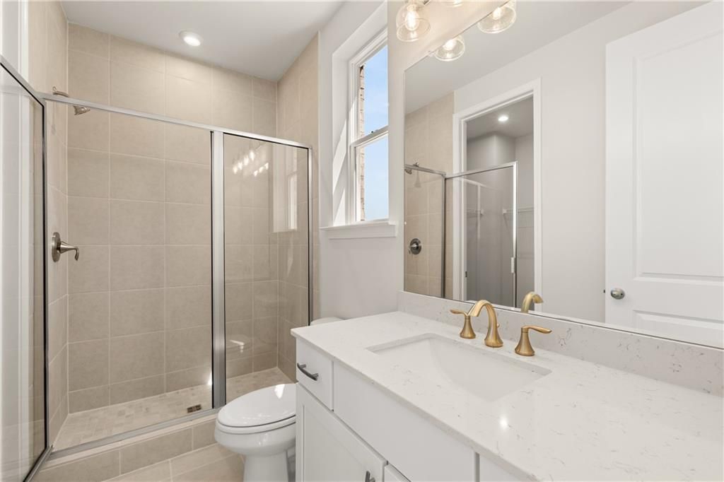 Modern bathroom with glass shower enclosure, beige tile, white quartz vanity, gold faucets in The Danbury C, Buford, Georgia
