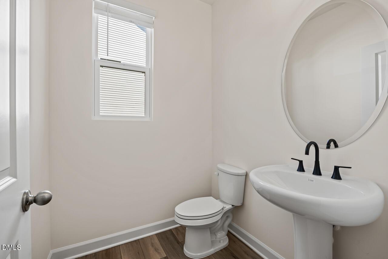 Bright half bath with pedestal sink, black faucet, round mirror, and toilet in Davidson Homes Hickory II B, Lillington NC