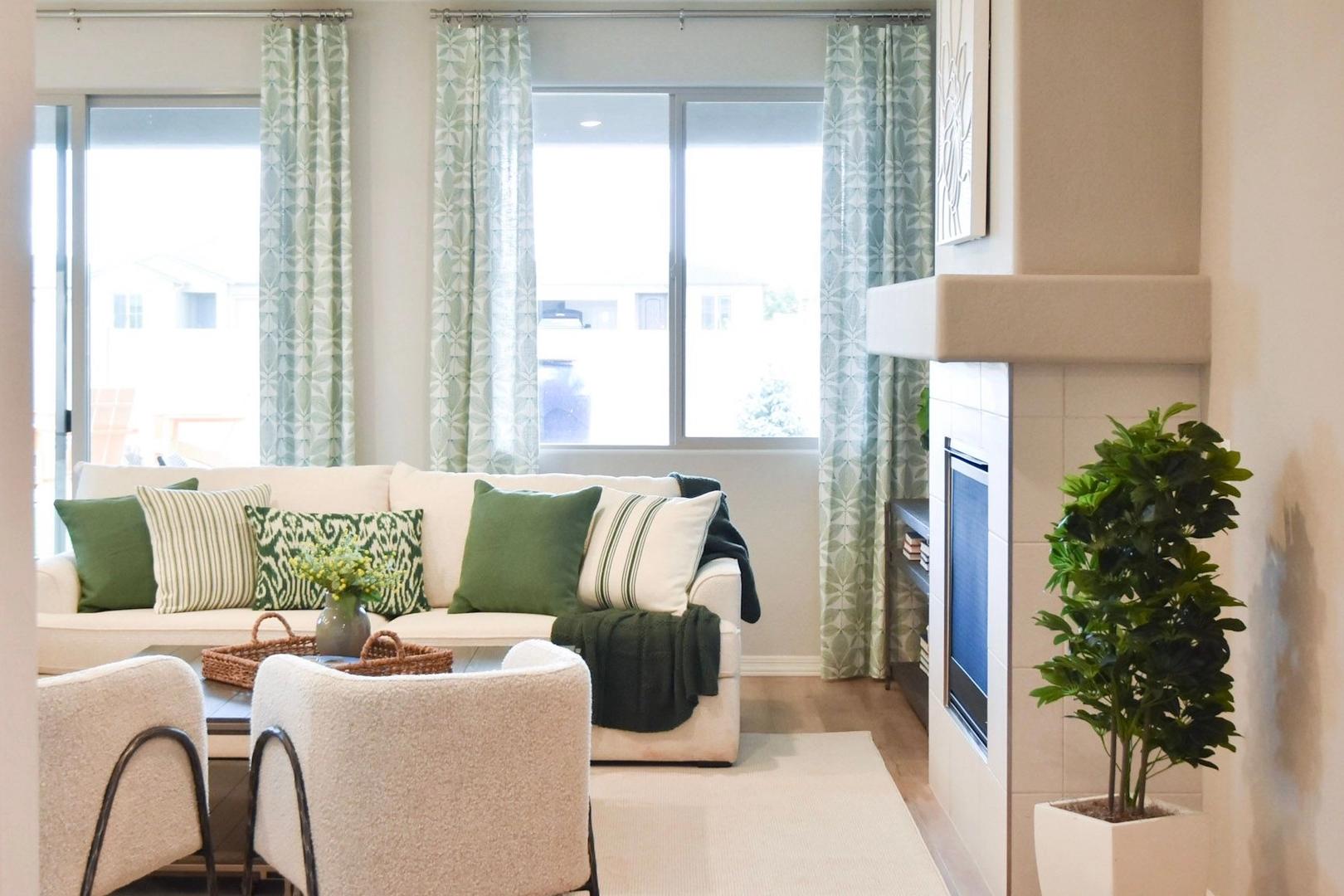 Cozy living room in The Harmony B Davidson Homes featuring gas fireplace, L-shaped sofa, large windows, and lush plants
