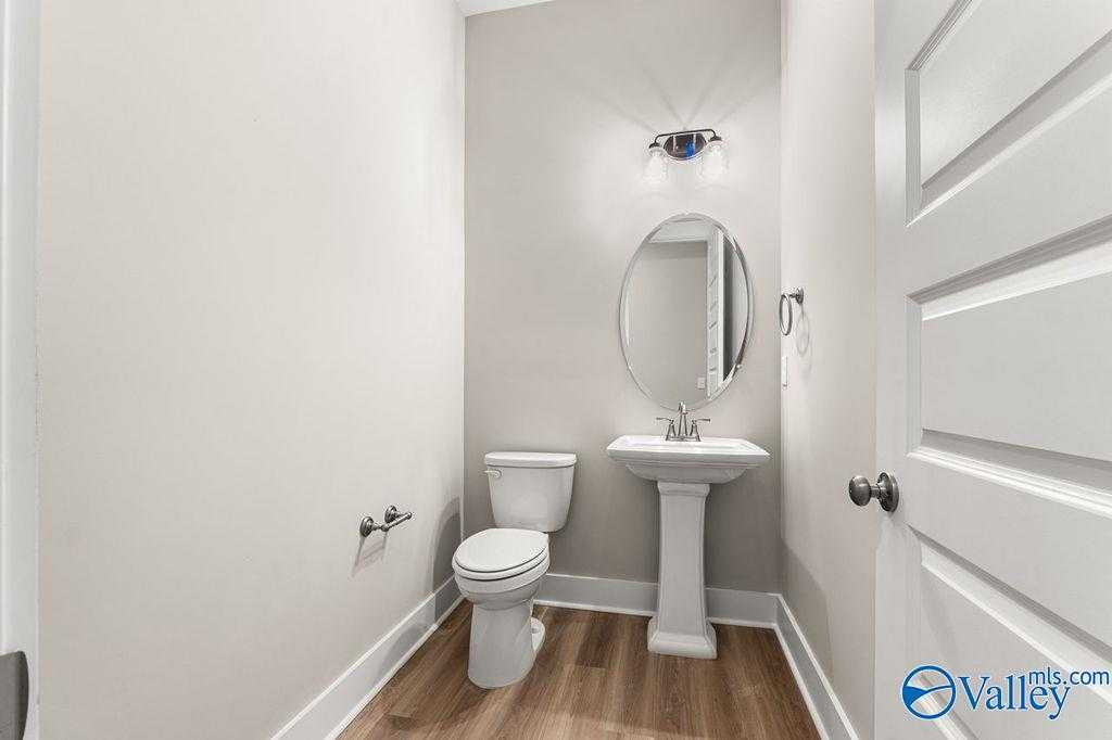 Elegant powder room featuring pedestal sink, round mirror, and neutral tones in 5-bedroom The Oxford home, Owens Cross Roads, Alabama