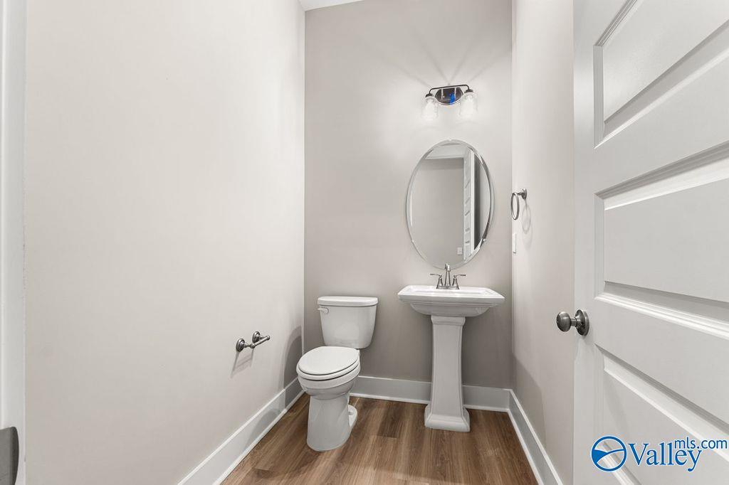 Elegant powder room with pedestal sink, round mirror, and toilet in Evermore Homes The Oxford, Owens Cross Roads, Alabama
