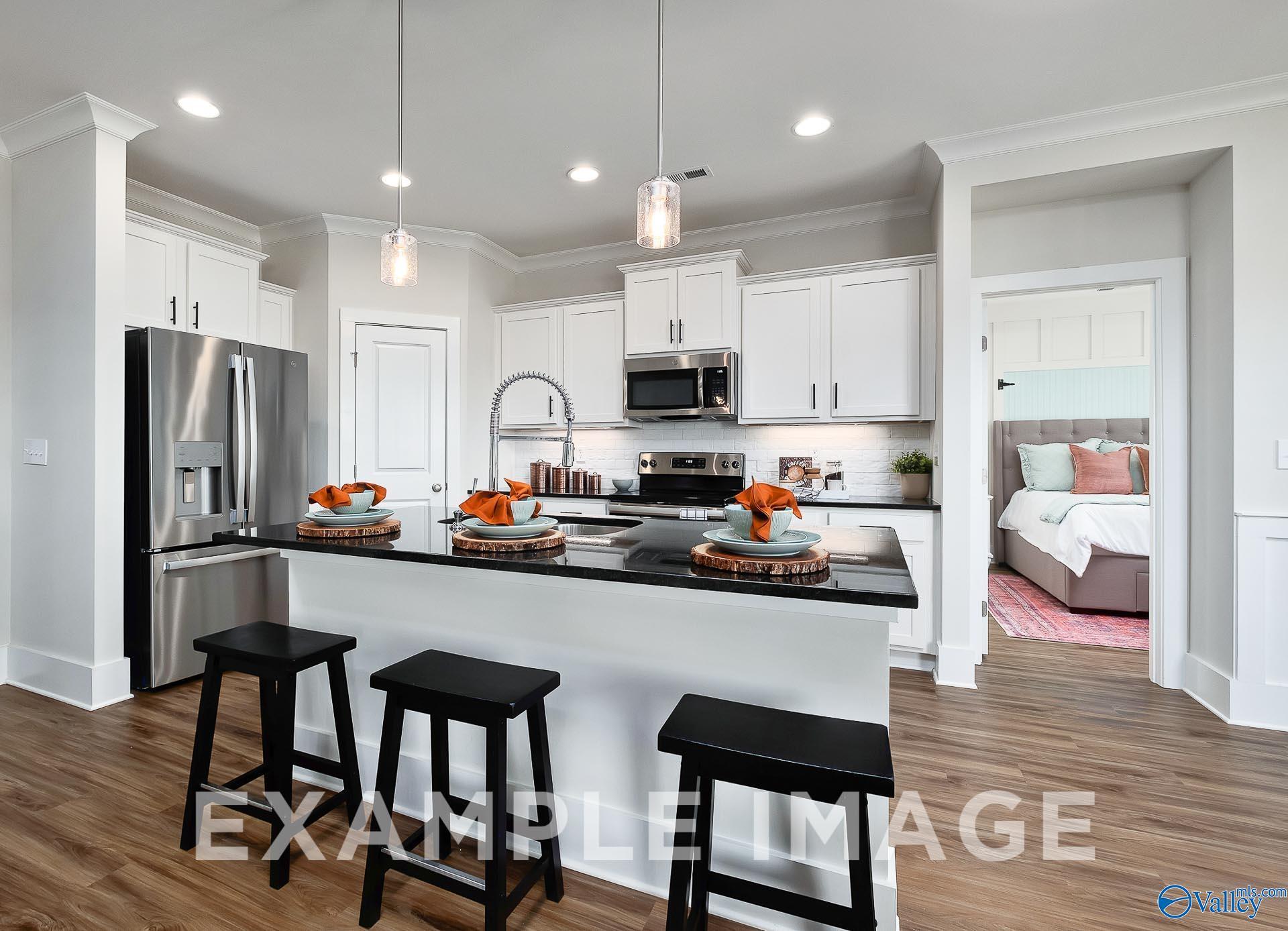 Modern kitchen with white cabinets, granite island, and stainless appliances in The Everett B home at The Meadows, Alabama.