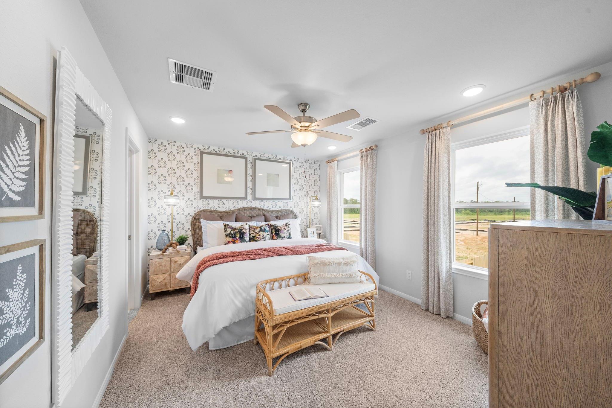 Bright primary bedroom with ceiling fan, rattan bench, and large windows in Davidson Homes' Trinity F plan, Splendora, TX