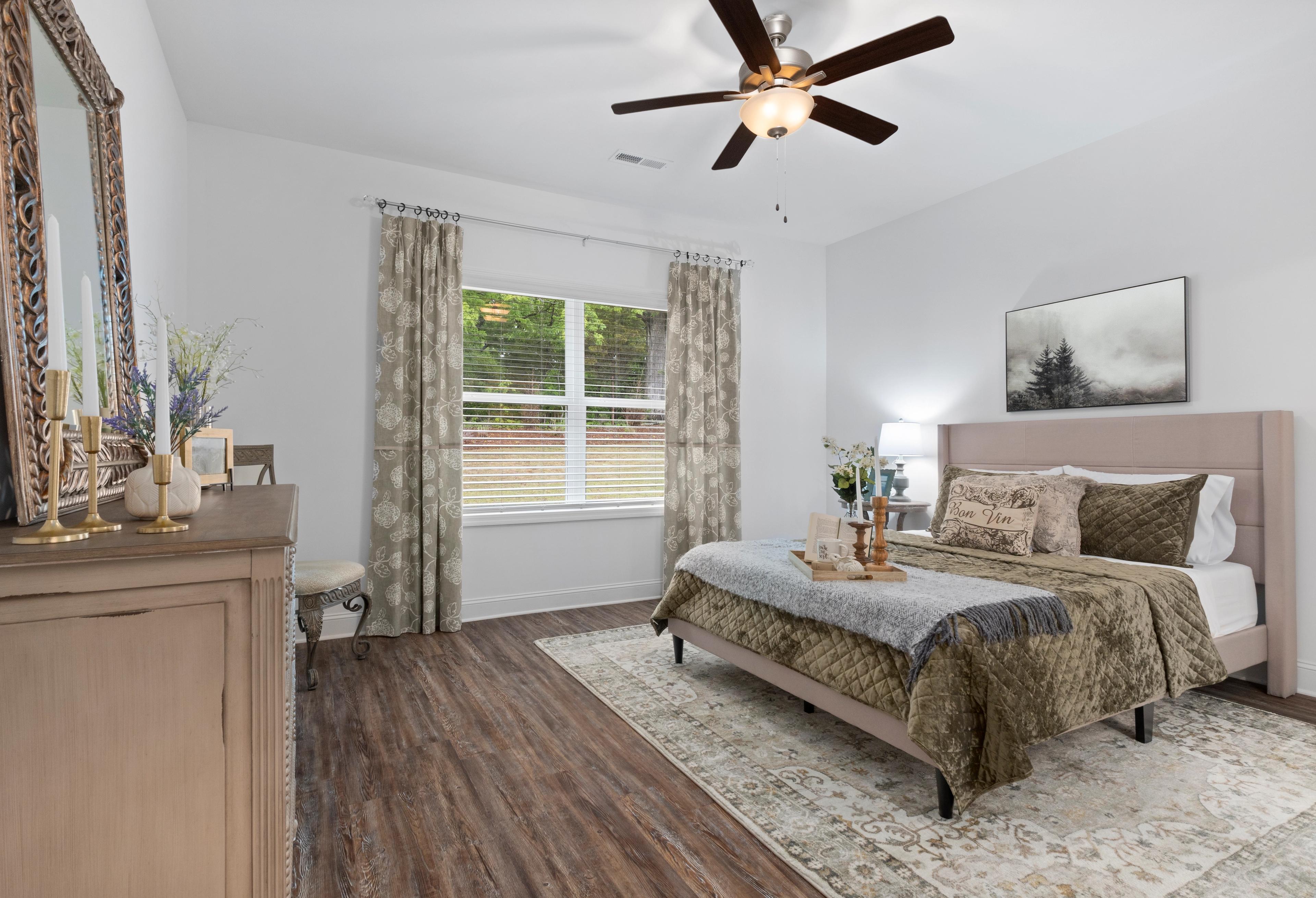Spacious master bedroom in The Cumberland: king bed with neutral bedding, wooden dresser, large window, ceiling fan, soft rug