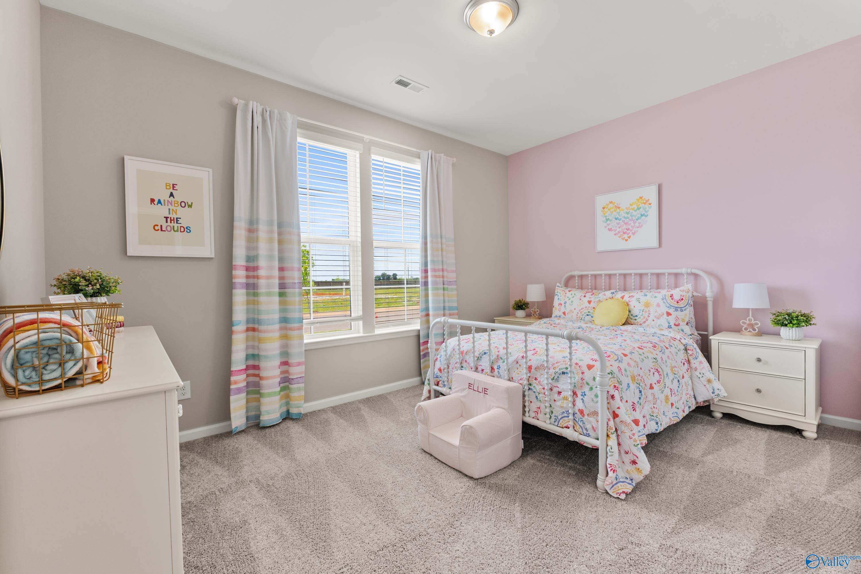 Adorable pink girl's bedroom with floral twin bed, colorful curtains, and window view in Davidson Homes The Sanctuary, Athens Alabama