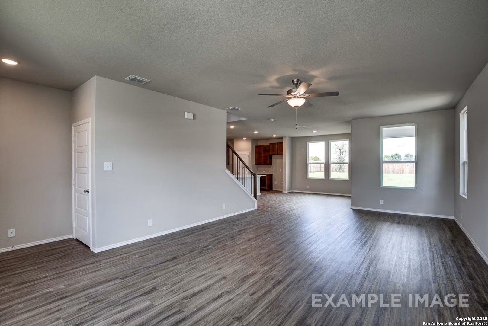 Spacious open living area with hardwood floors, ceiling fans, and staircase in 4-bedroom The Murray K home, Comanche Ridge, San Antonio