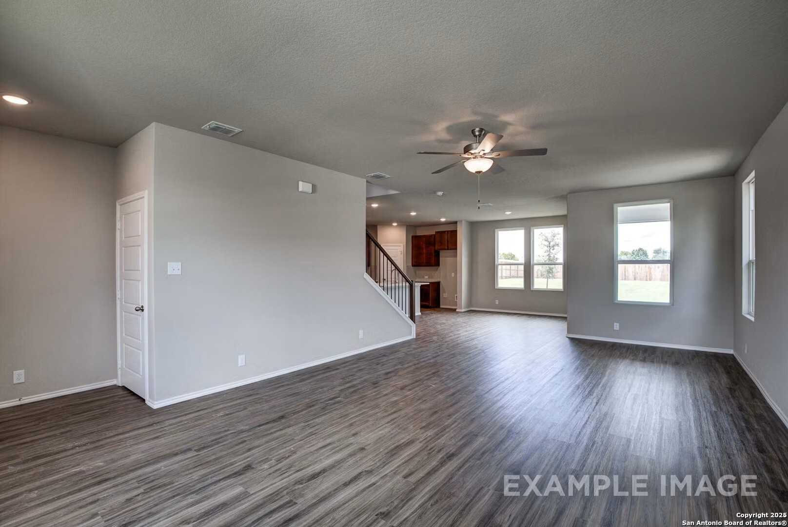 Spacious open living area with hardwood floors, ceiling fans, and staircase in 4-bedroom The Murray K home, Comanche Ridge, San Antonio